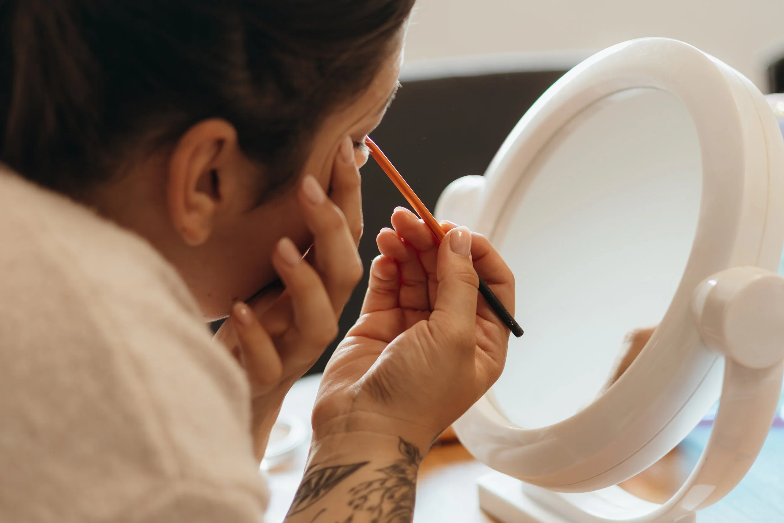 Frau trägt Make-up auf ihr Augenlid vor einem Spiegel auf einem Tisch.