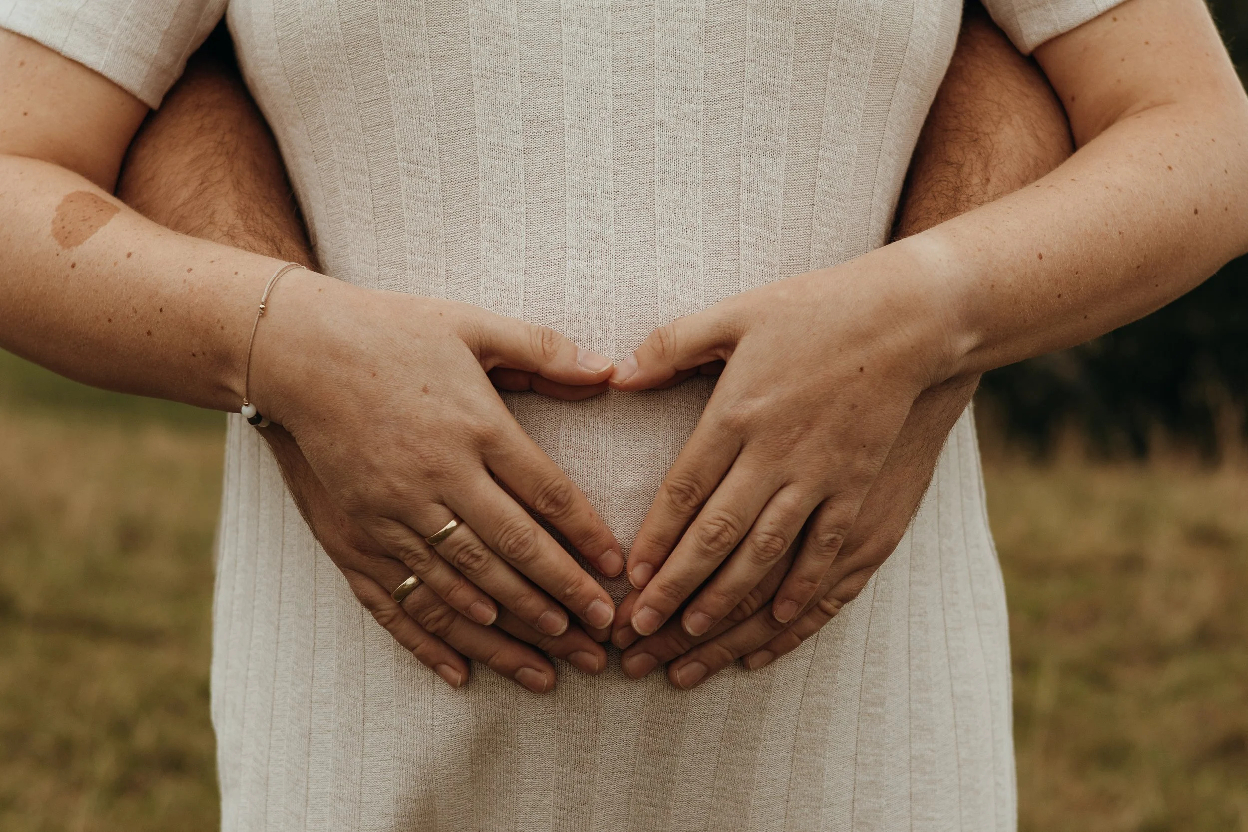 Zwei Paare legen ihre Hände auf den Babybauch und formen ein Herzzeichen.