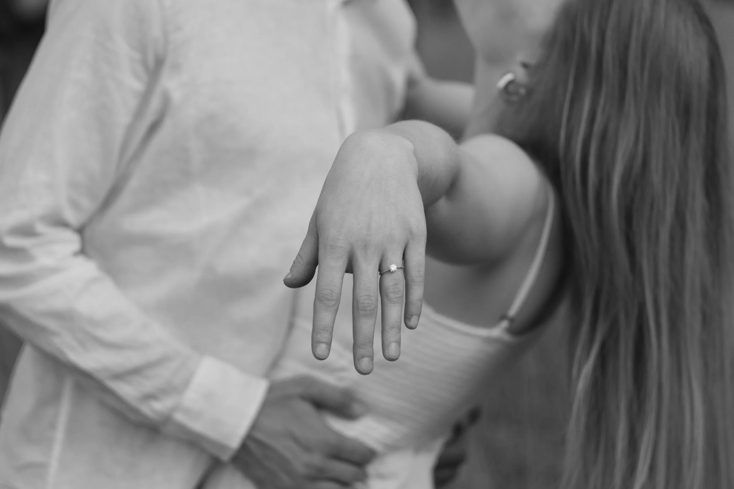 Nahaufnahme eines Paares, das eine schwangere Frau in einem Krankenhaus hält, wobei die Hand der Frau mit einem Verlobungsring sichtbar ist.