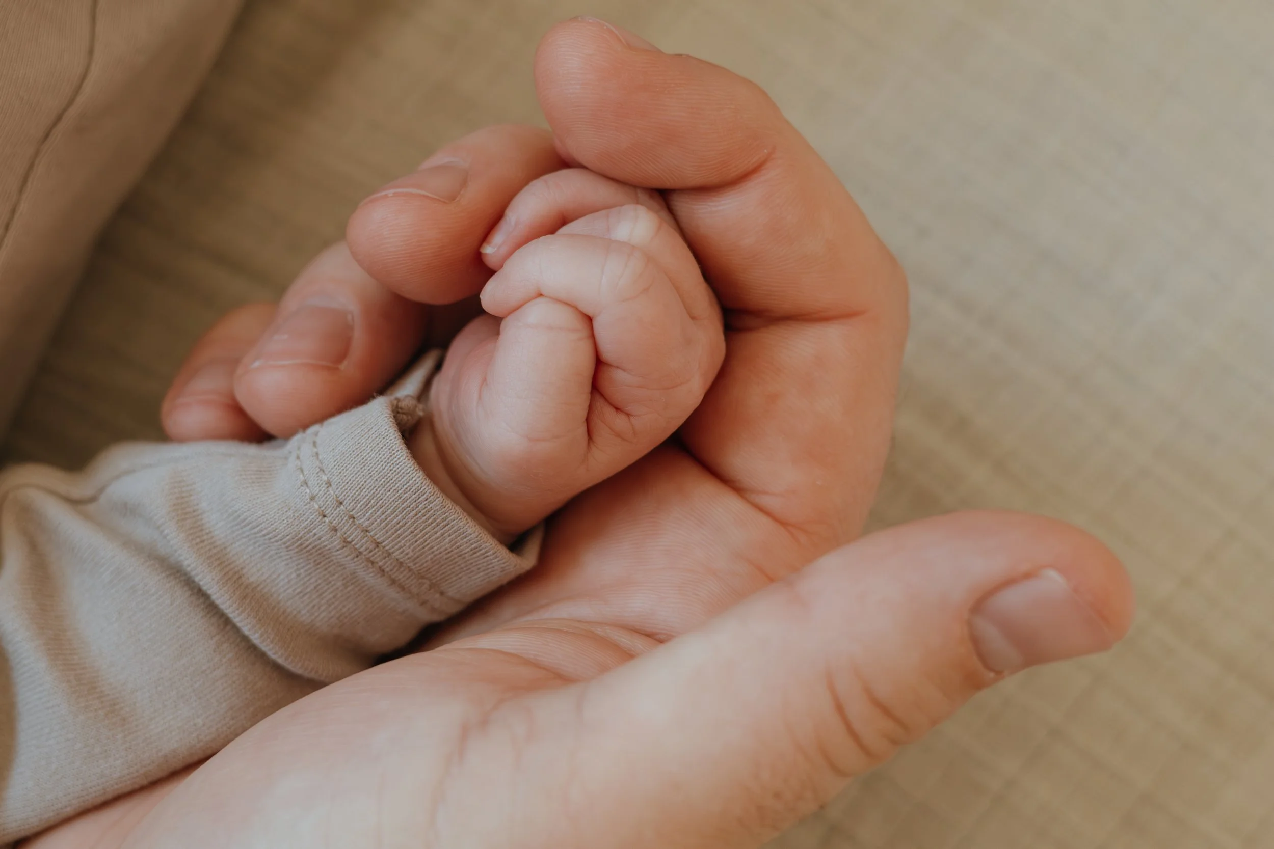 Nahaufnahme von einer Erwachsenenhand, die ein Baby-Crayon hält, beide Hände verschränkt, mit einem neutralen Hintergrund.