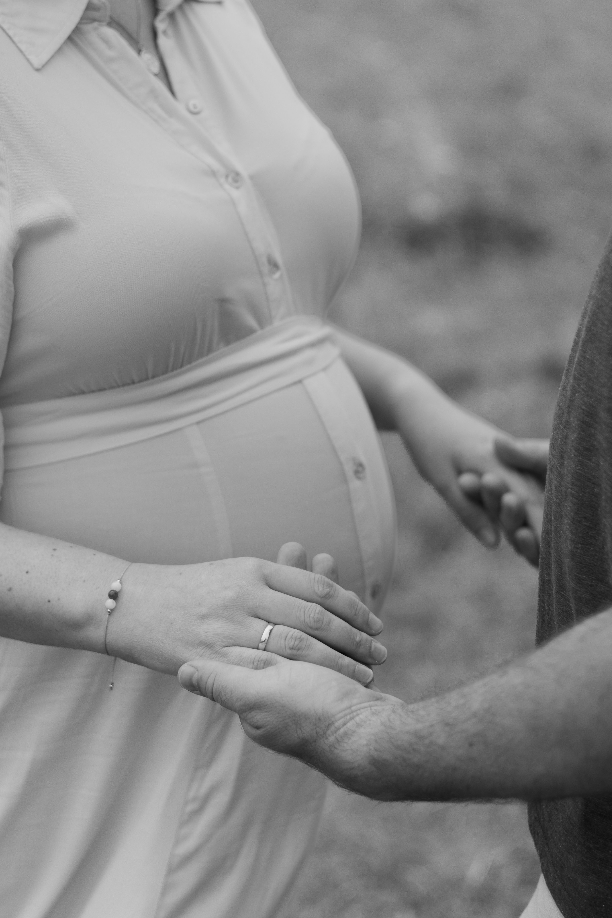 Schwangere Frau hält Hand eines Partners bei einer outdoor Familienszene, schwarz-weiß