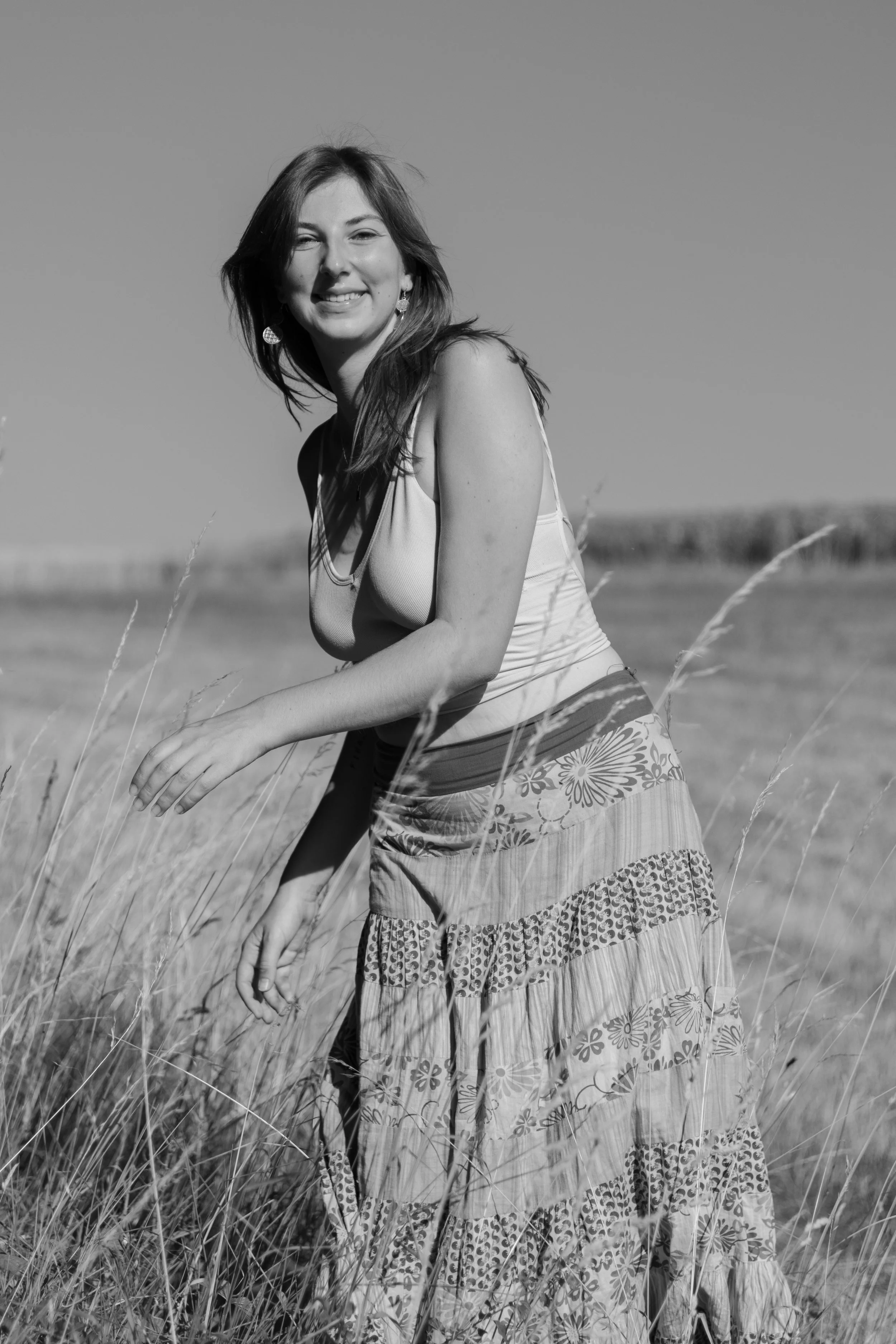 Schwarz-weiß Bild einer lachenden jungen Frau in einem langen Rock, die im Feld steht.