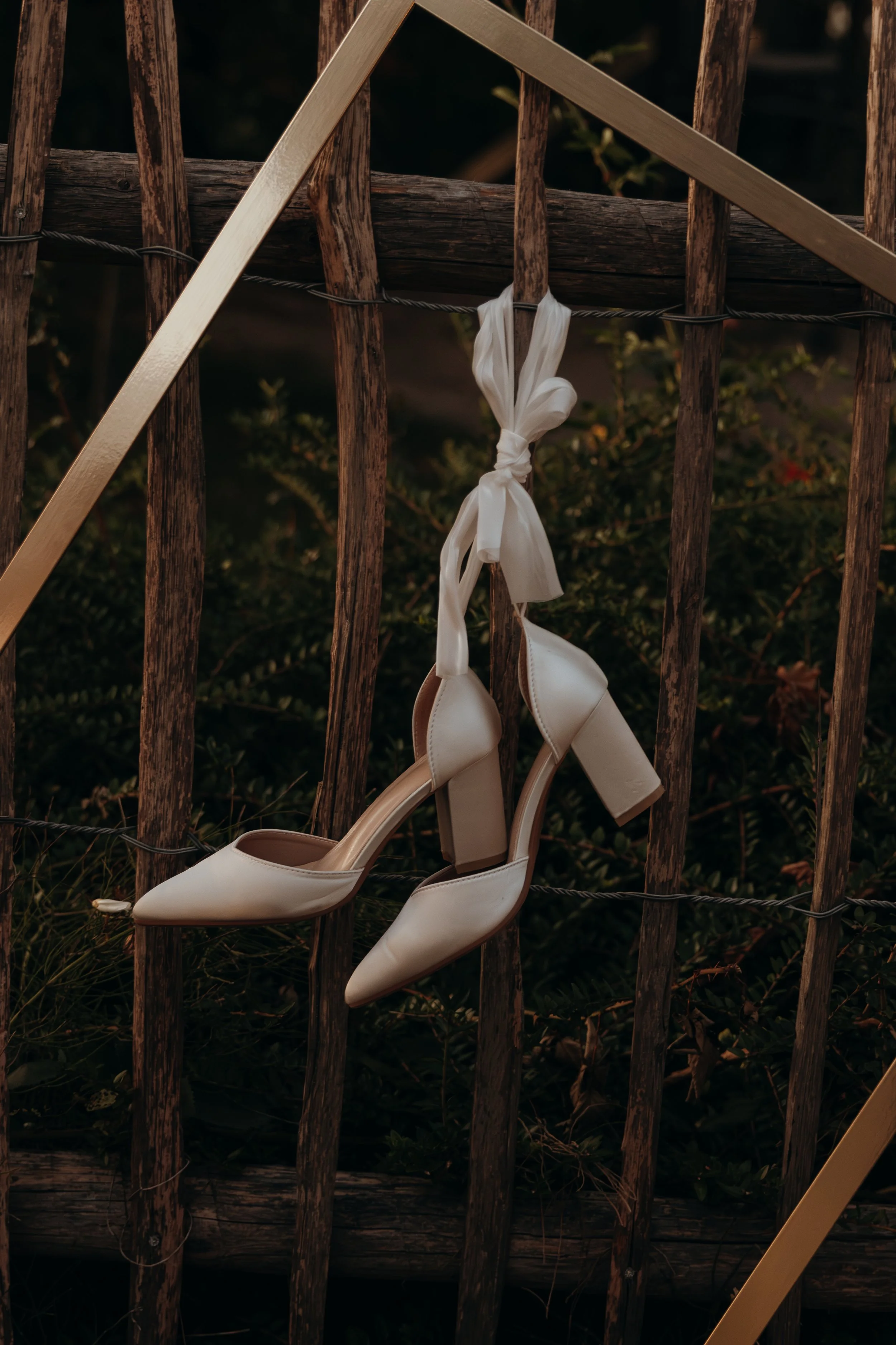 Weiße High Heels mit Knoten am Schnürsenkel hängen an einem Holzgitter im Freien.