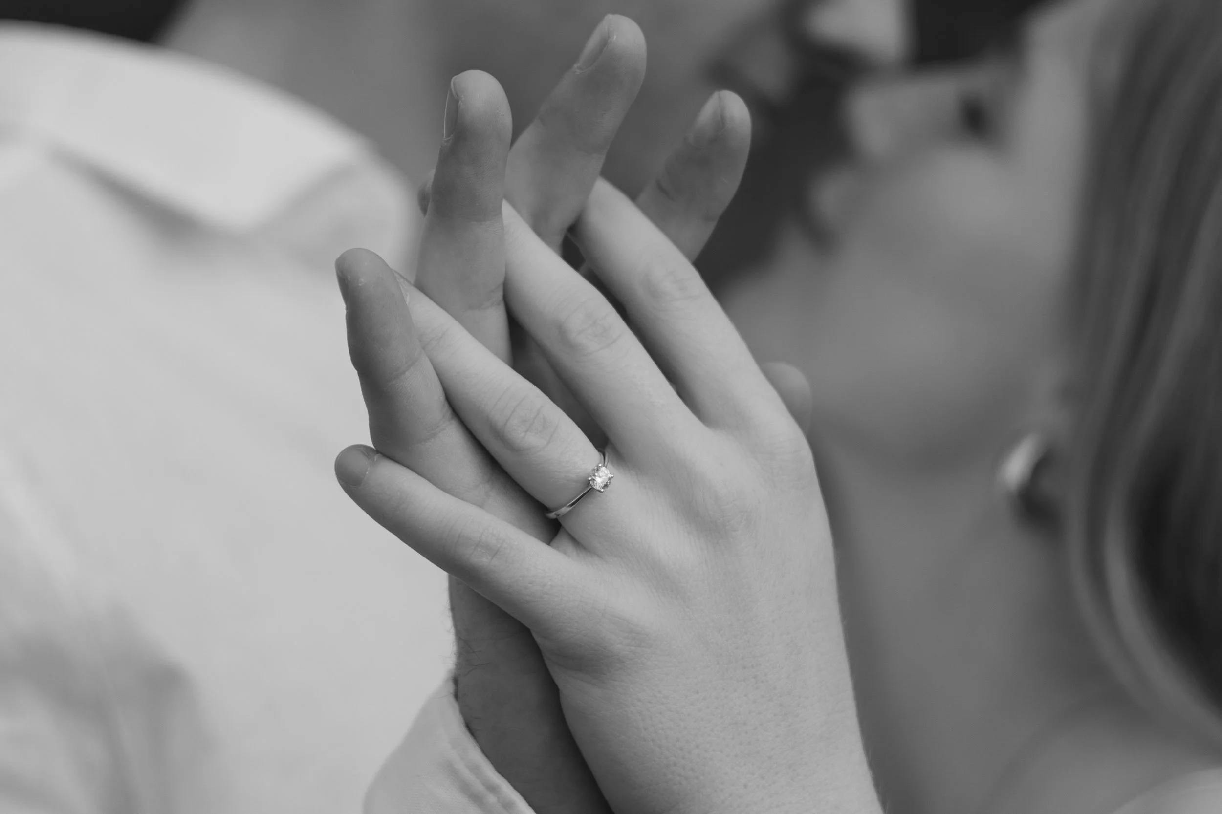 Zwei Hände, die sich berühren, eine mit einem Verlobungsring mit Diamant, in Schwarz-Weiß fotografiert.