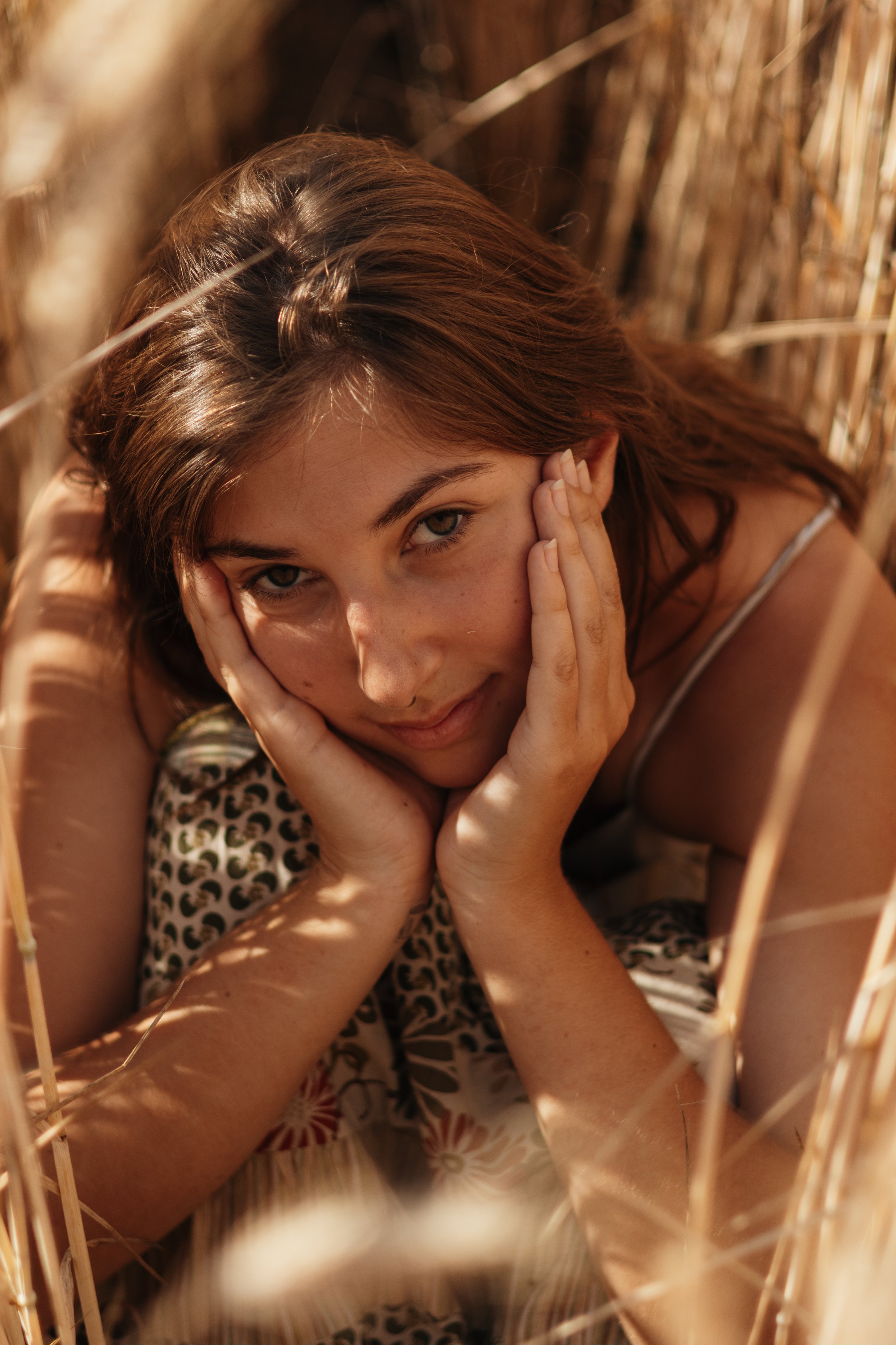 Junge Frau liegt in einem Weizenfeld, schaut direkt in die Kamera, trägt ein Leopardenmuster-Top, hat braune Haare, und ist in natürlichem Sonnenlicht gefilmt.