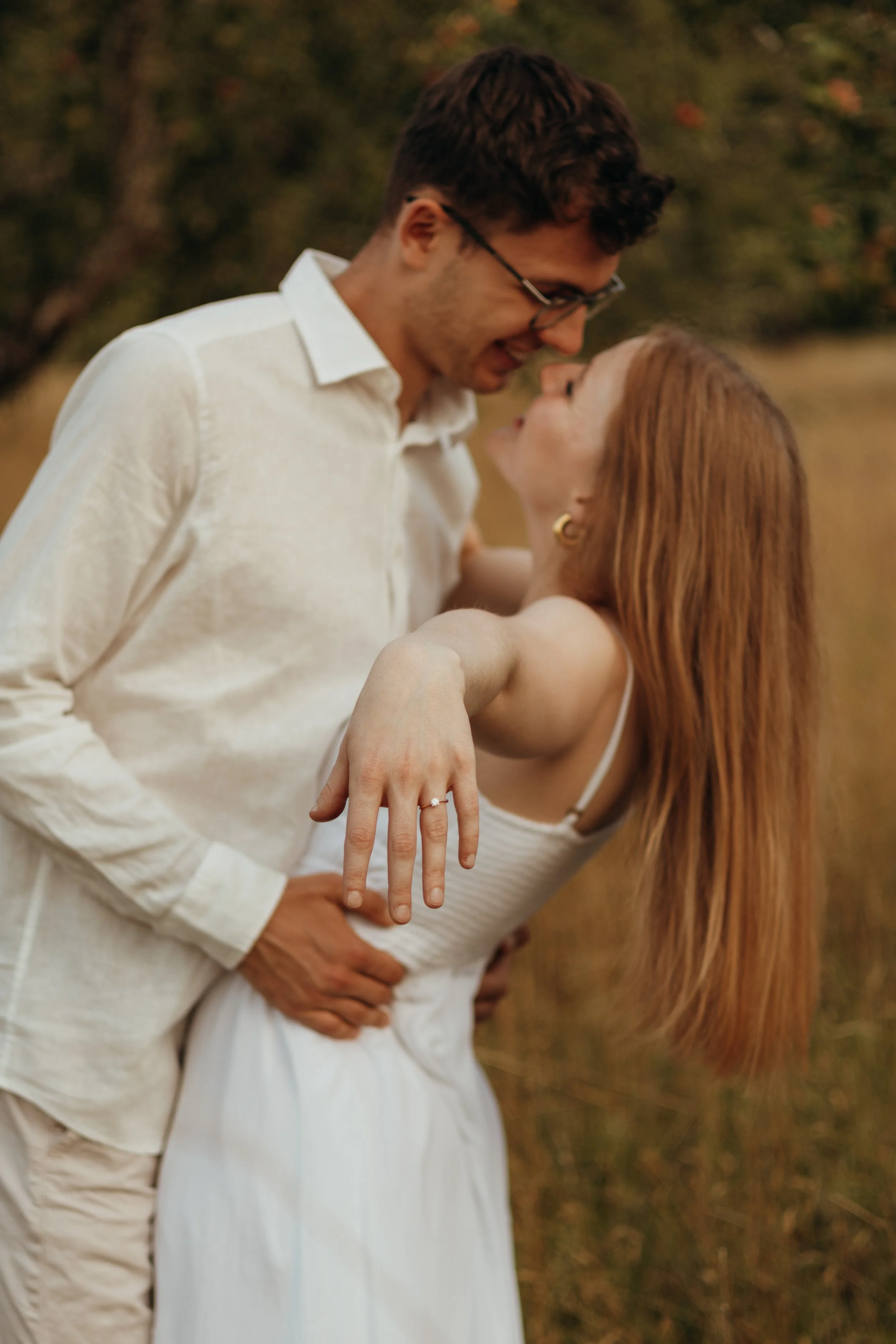 Ein Paar in einer romantischen Umarmung im Freien, die Frau zeigt einen Ring an ihrer Hand.