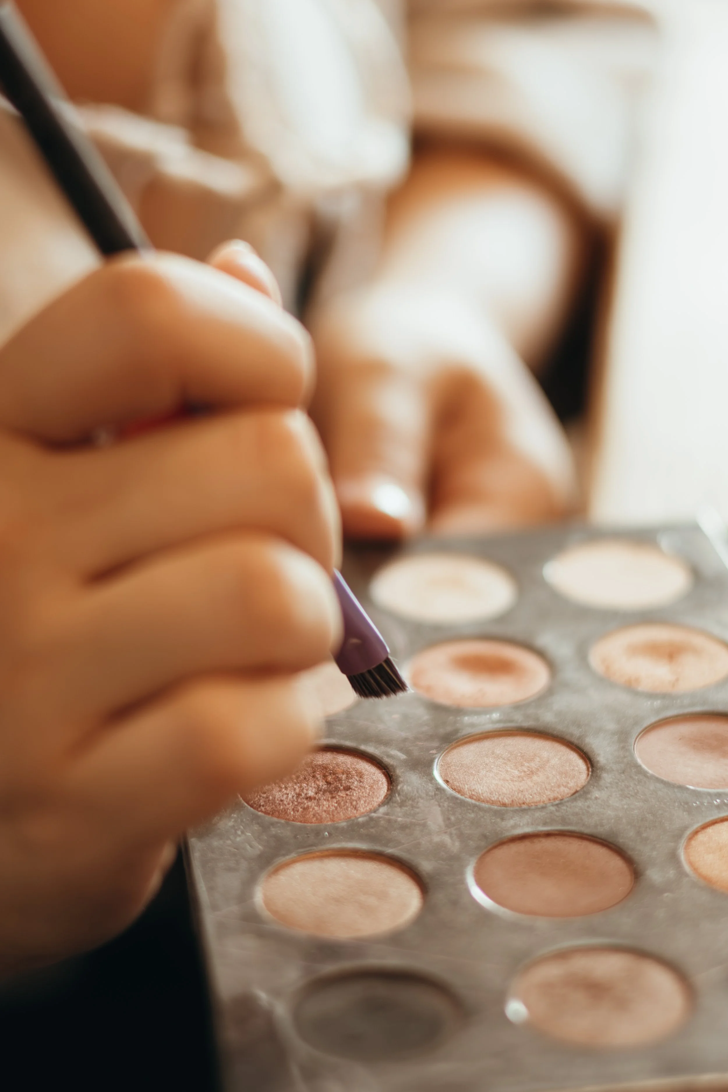 Hand hält Pinsel über Lidschattenpalette mit verschiedenen neutralen Tönen