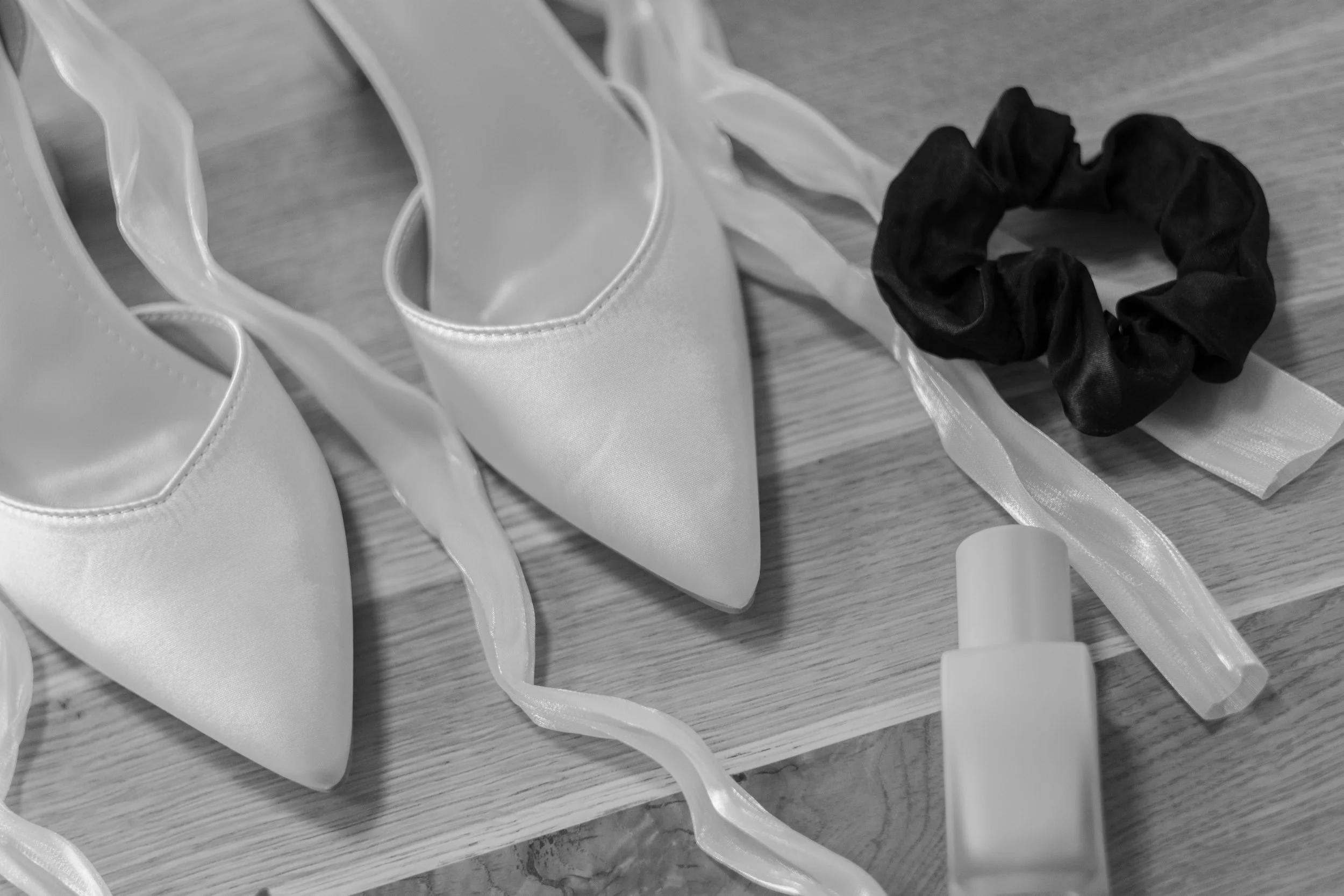 Weiße High Heels, eine schwarze Haarspange, ein Haarspray und ein Haarband auf einem Holztisch.