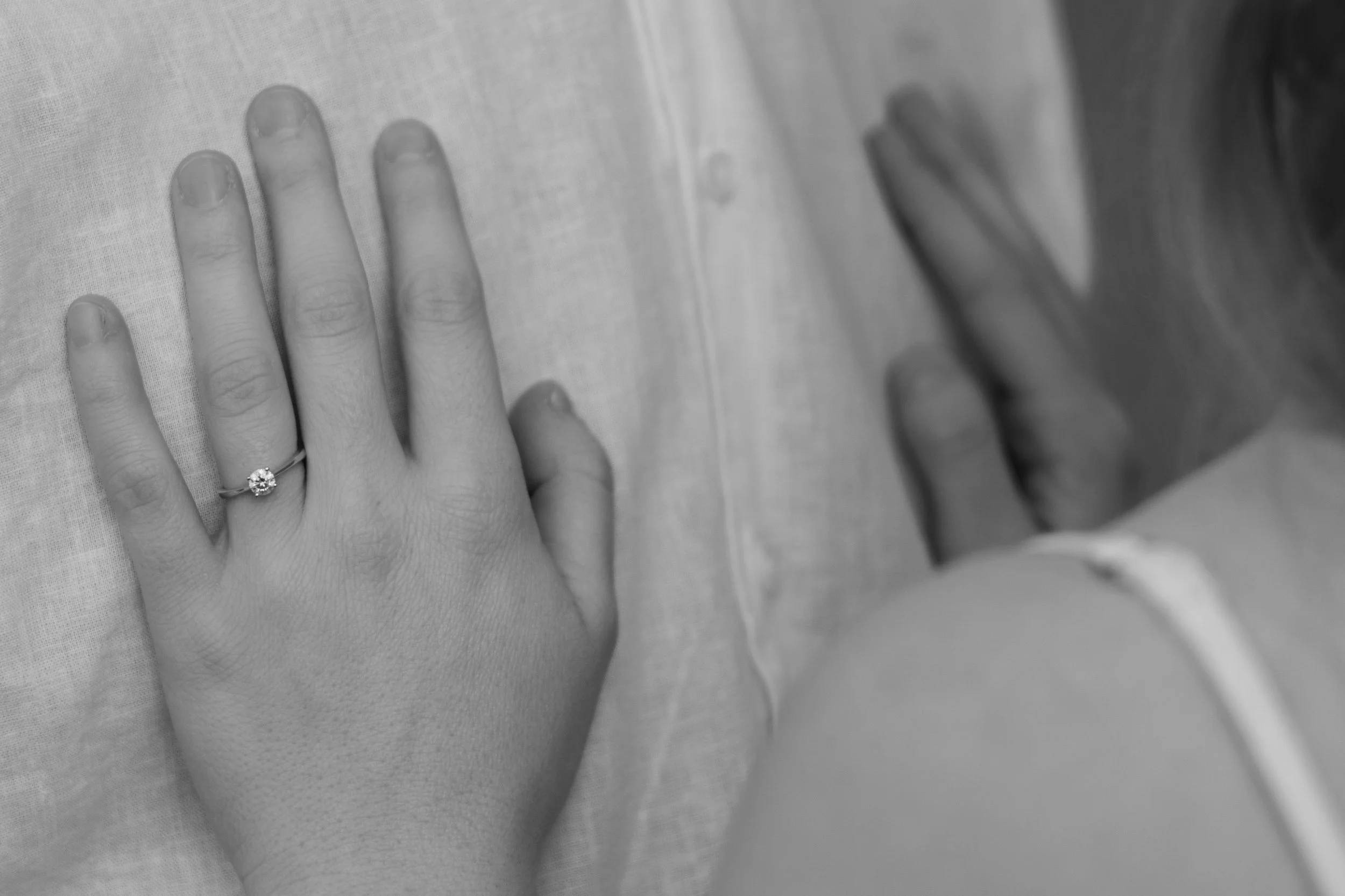 Eine Hand mit Ehering liegt auf einem Stoffbett, neben weiteren Händen, eine davon mit einer Lätzchen-ähnlichen Verbindung.