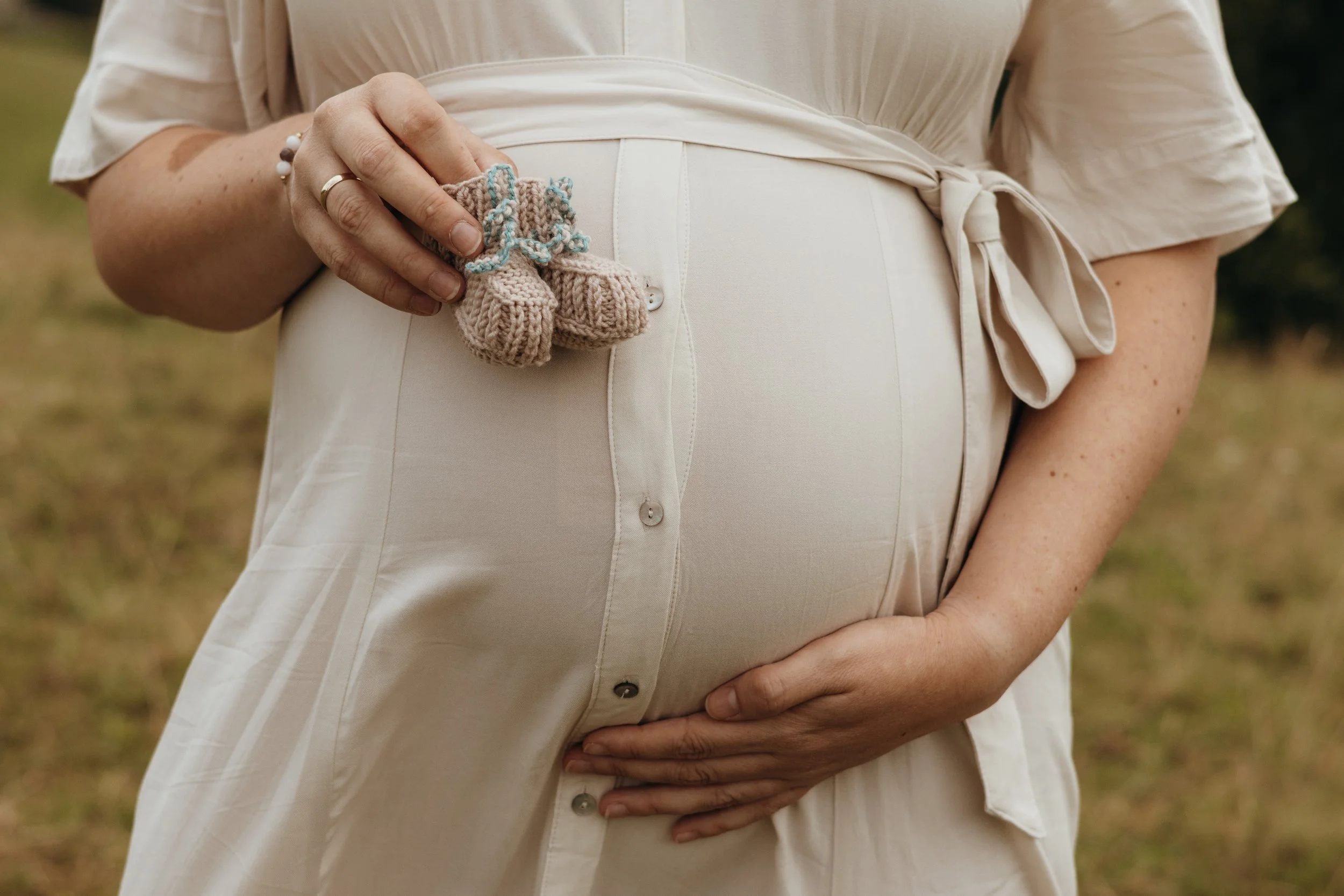 Schwangere Frau hält kleine, gestrickte Babyschuhe bei sich.