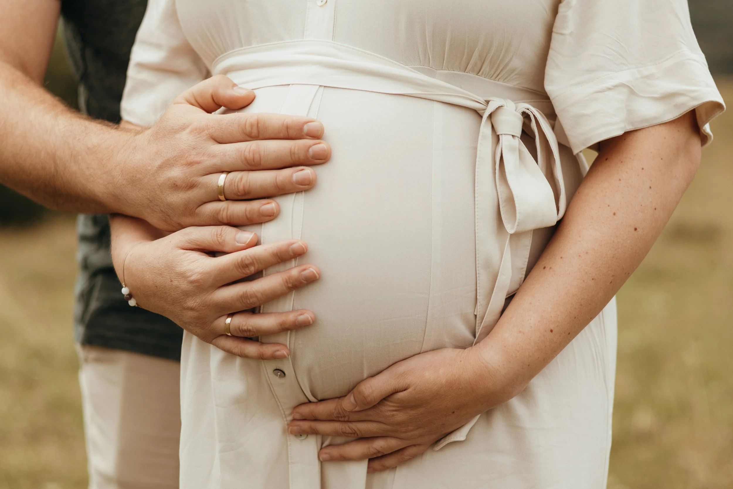 Nahaufnahme eines schwangeren Frauenbauchs, auf dem Hände eines Mannes und einer Frau liegen, die ihn sanft halten.