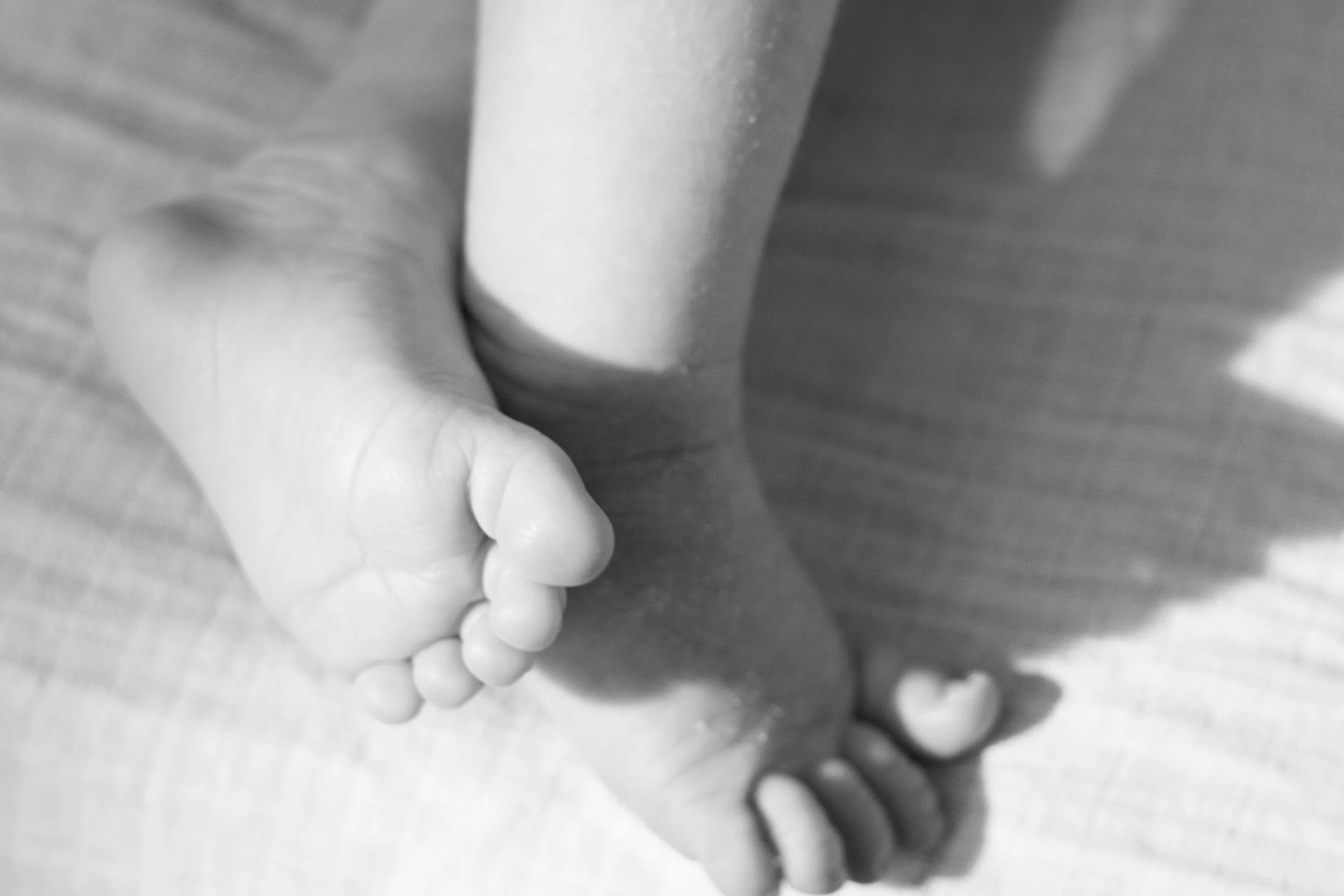 Nahaufnahme eines Kindes, das an einem Boden aus Holz sitzt und seine Füße berührt.