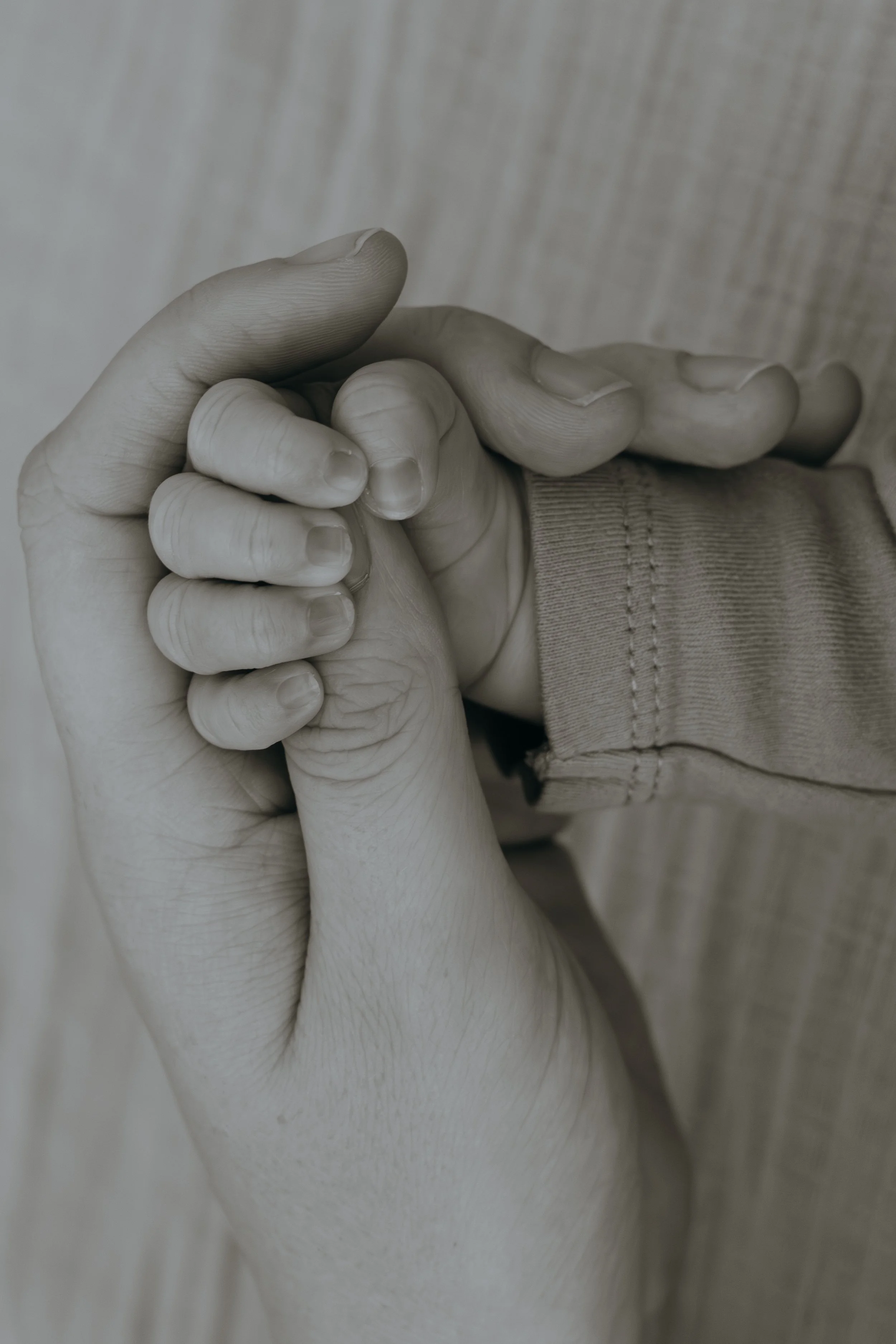 Nahaufnahme von einer erwachsenen und einer kindlichen Hand, die sich gegenseitig festhalten.