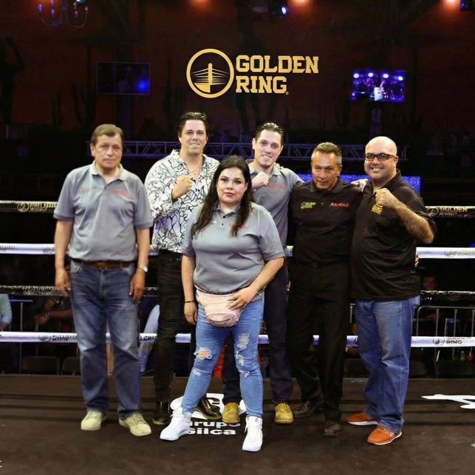 Six people standing inside a boxing ring at Golden Ring event, posing for a group photo, with a large Golden Ring logo on the background.