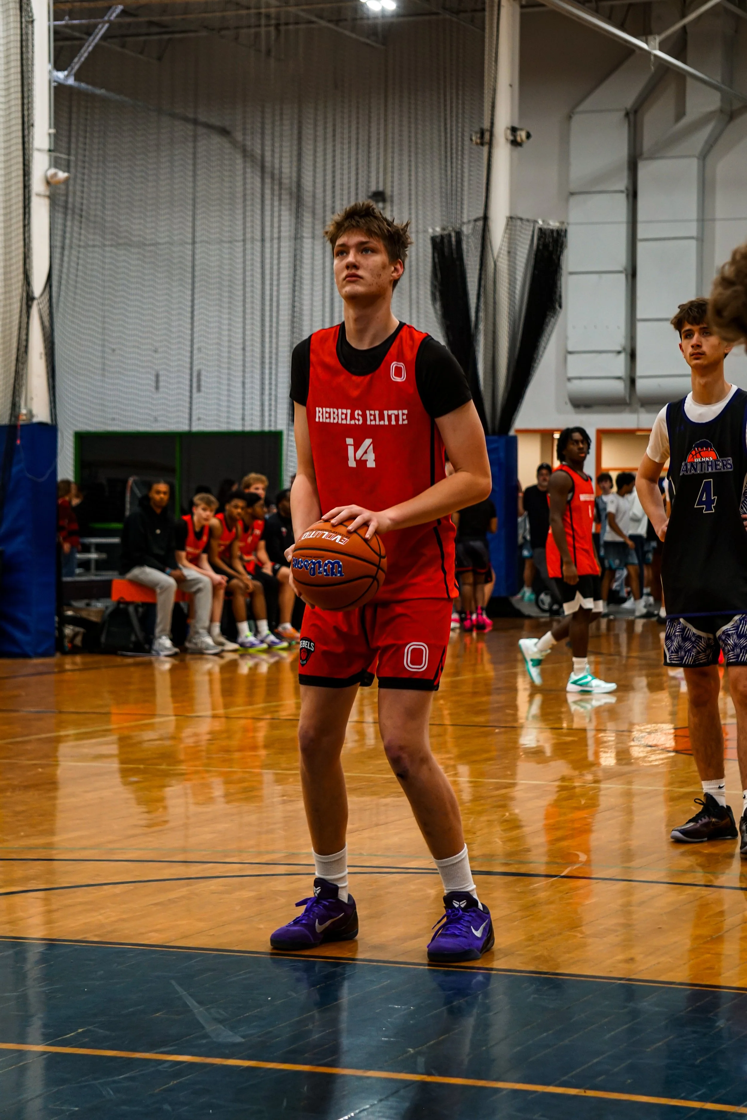 A young man in a white and red basketball uniform is preparing to shoot a basketball while being guarded by a player in a blue and black uniform during a game.