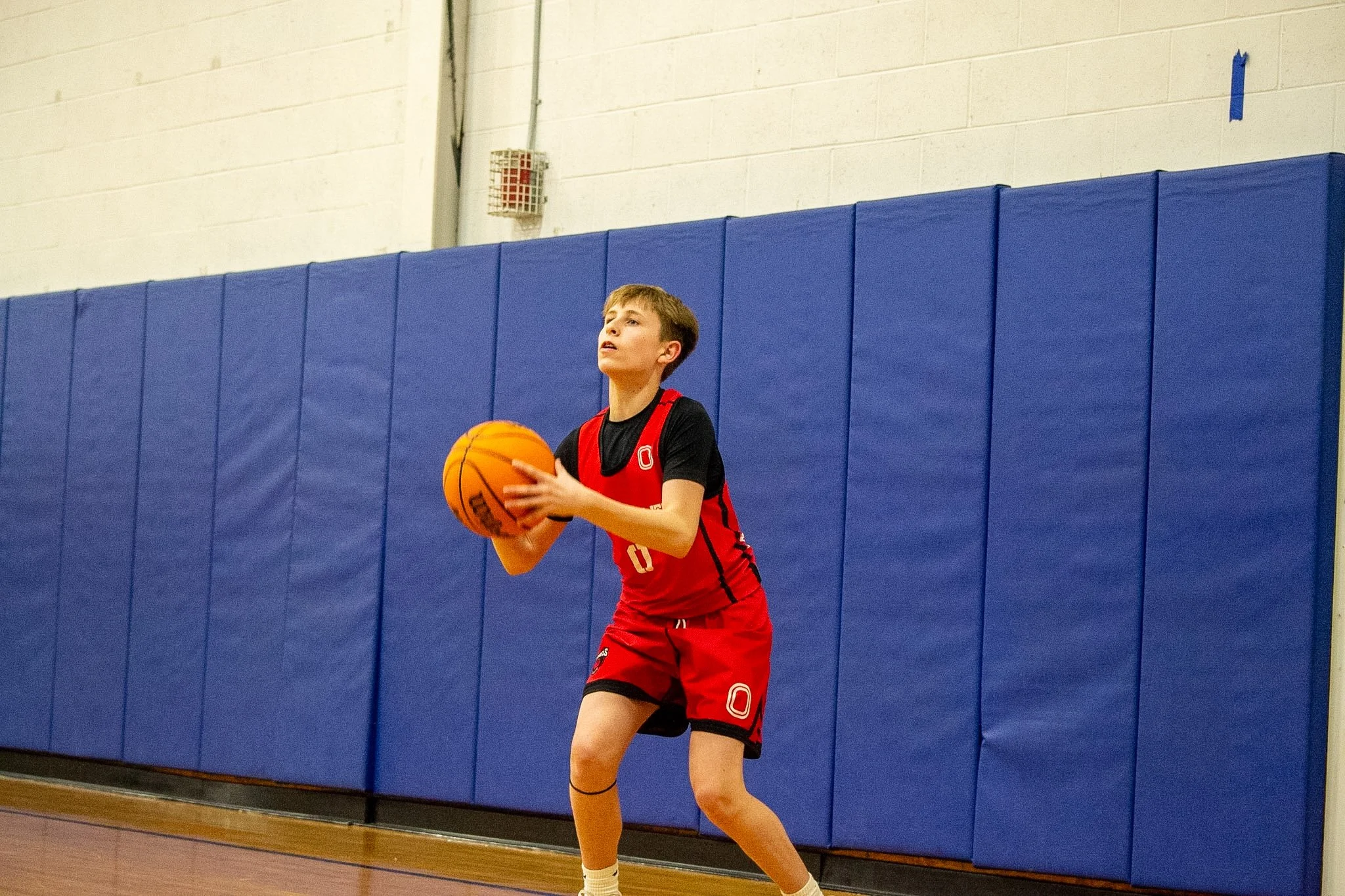 A young male basketball player walking on an indoor court, wearing a white and black jersey with red accents, number 3, and black shorts with red and white details.