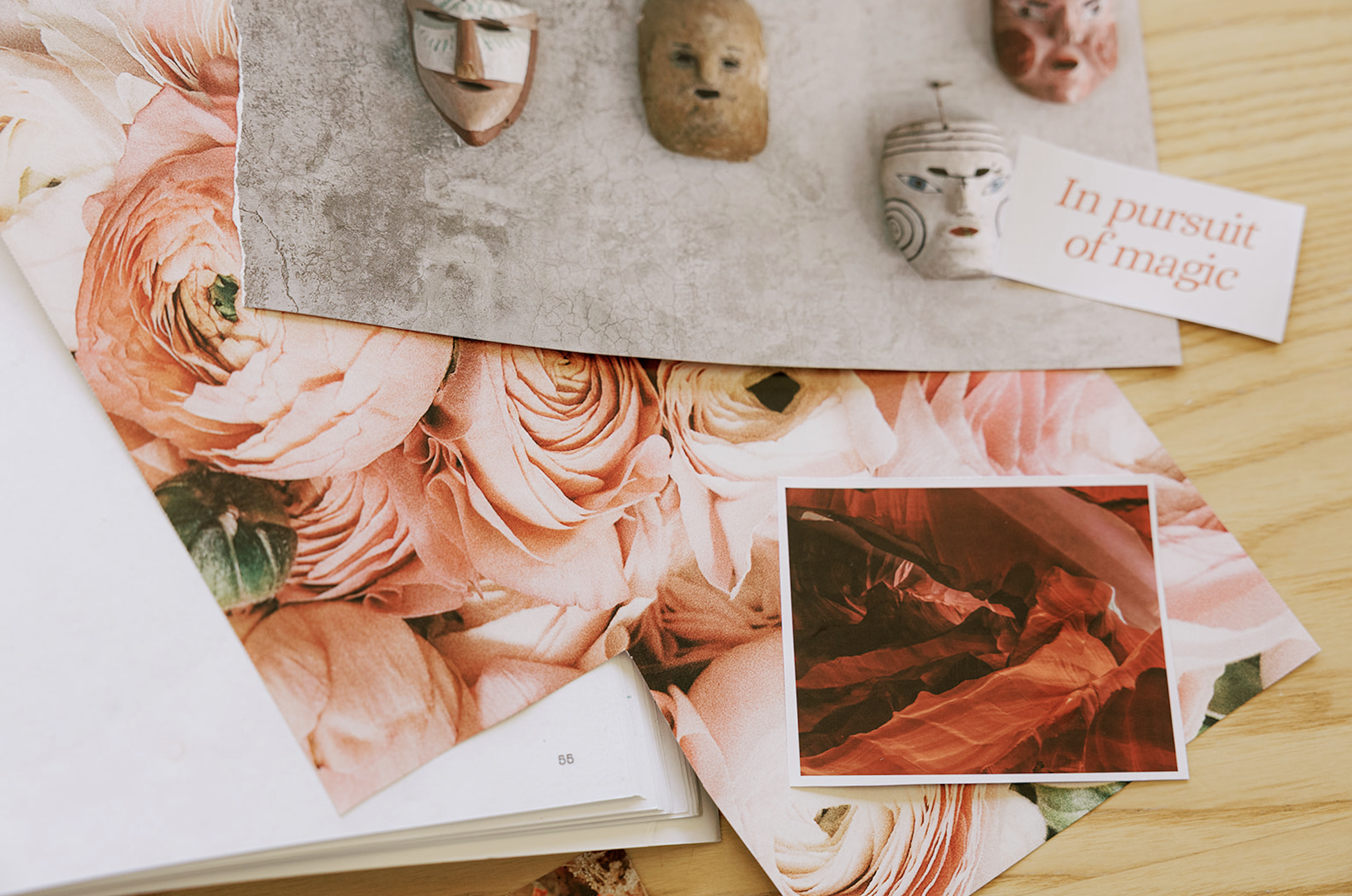 Arranged art and craft items including small face masks, a framed photo of red rock formations, an open book with floral print paper, and a card with red text on a wooden surface.