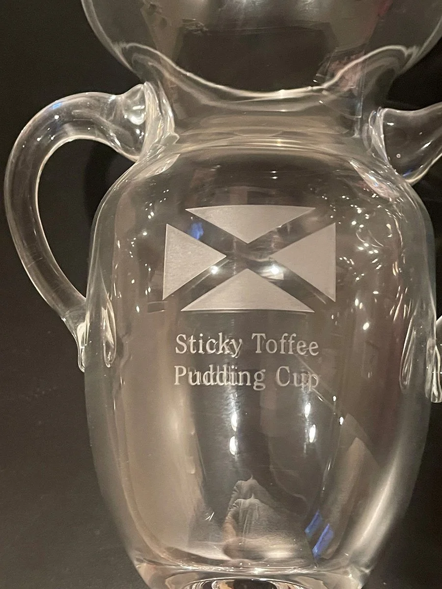 Clear glass jug with a handle, engraved with a logo and the text 'Sticky Toffee Pudding Cup'.