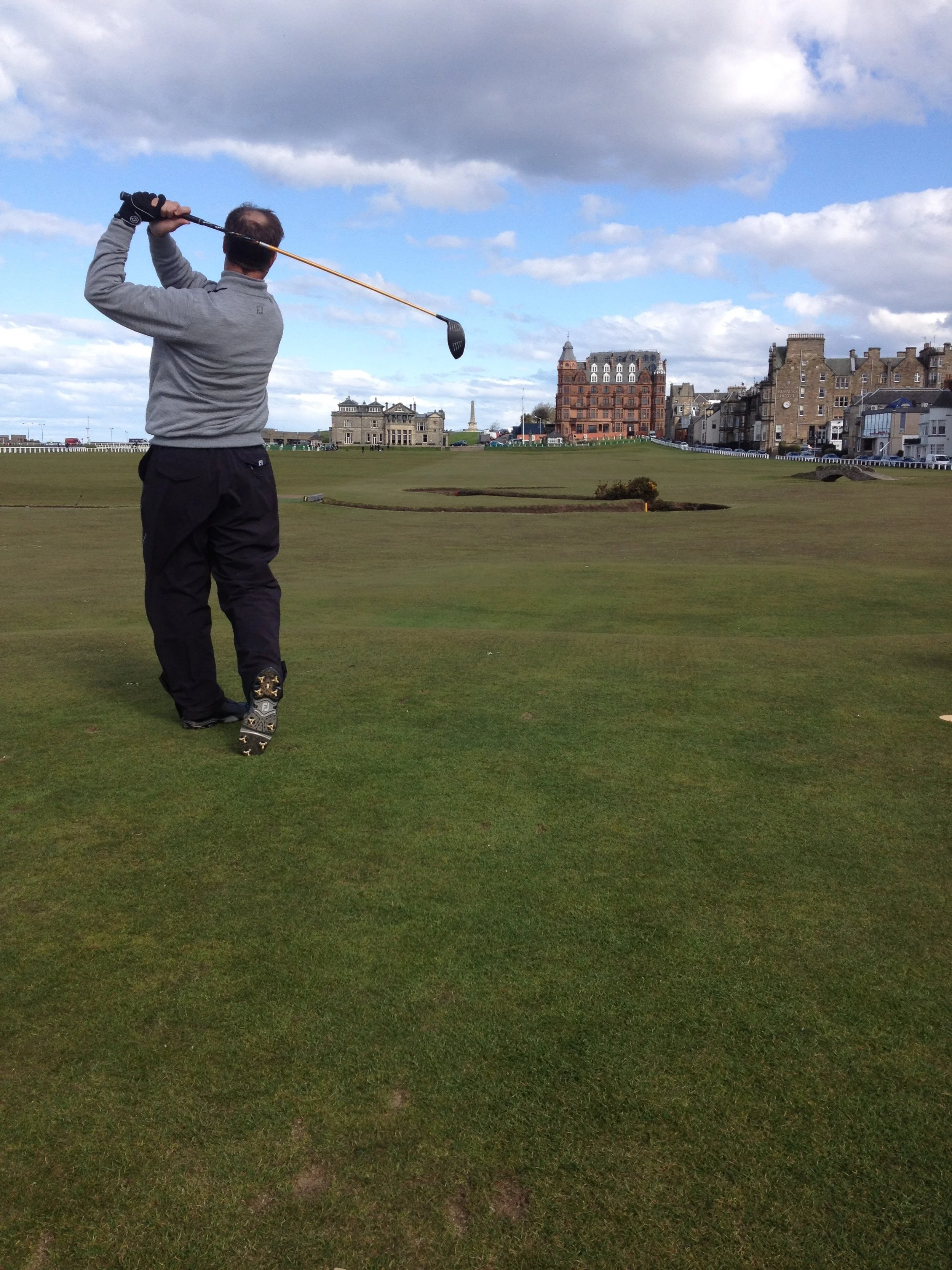 A man playing golf on a golf course, with a cityscape and cloudy sky in the background.