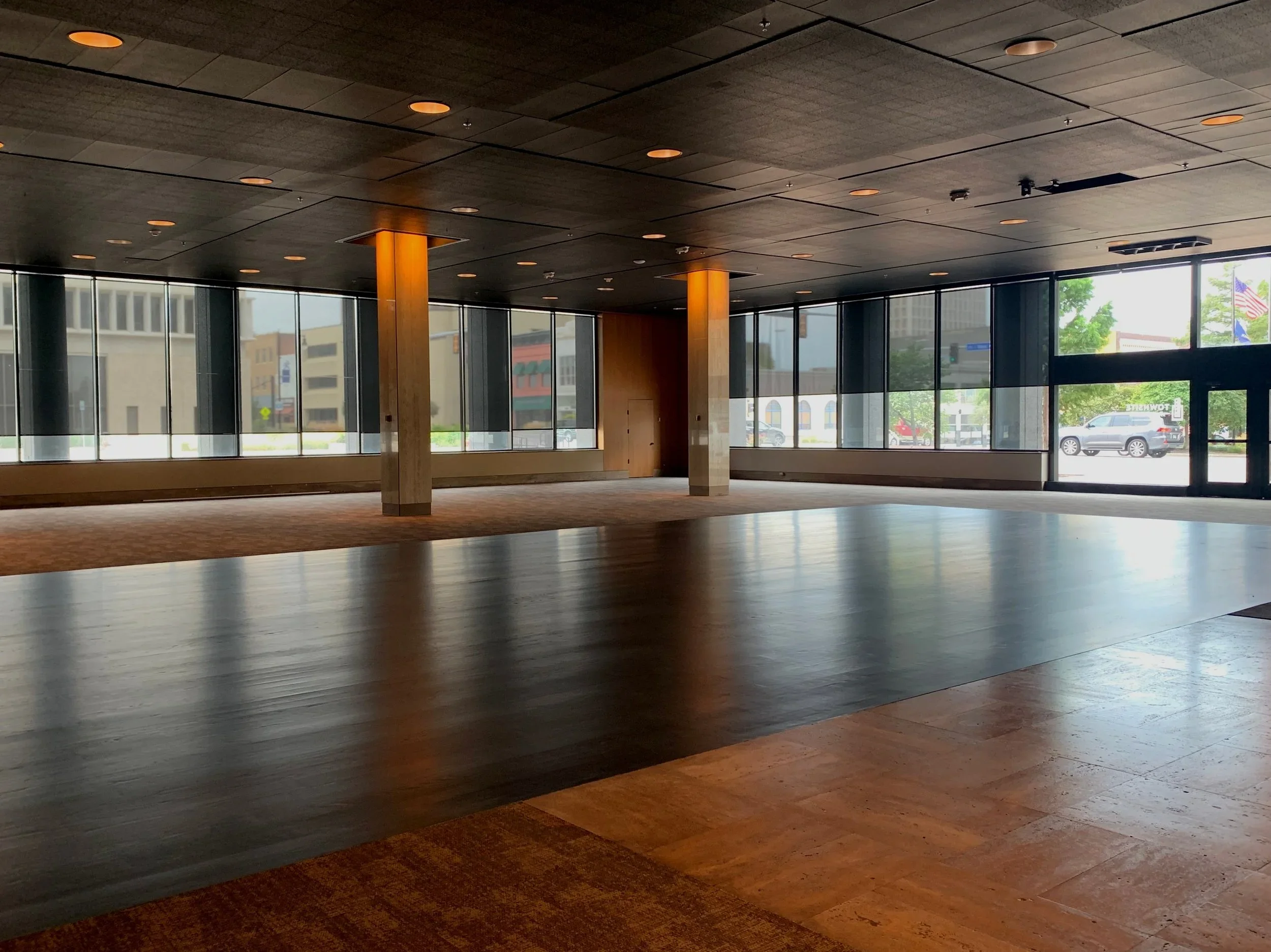 Empty interior of a modern commercial space with large glass windows, dark ceiling, wooden pillars, and mixed wood flooring.