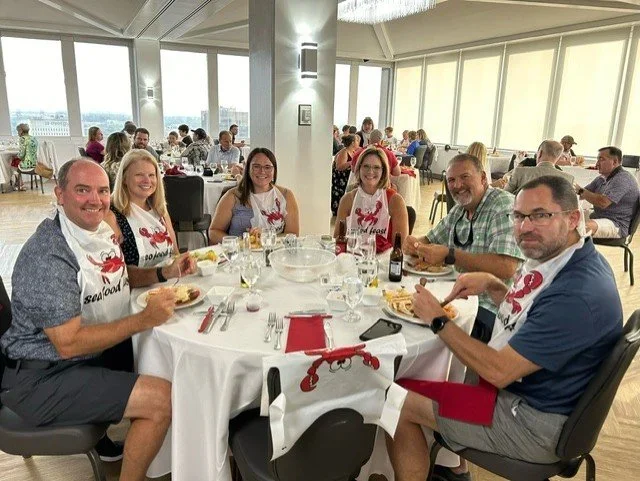 Six people in lobster-themed aprons around a dinner table.