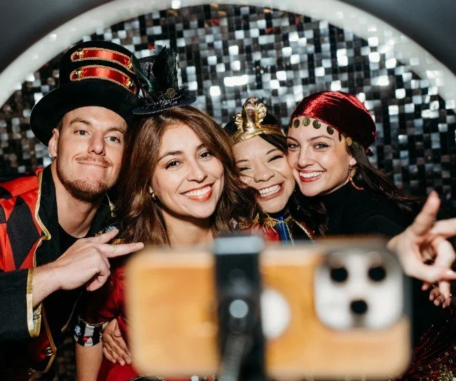 Four people in costume taking a selfie in front of a glittery backdrop.
