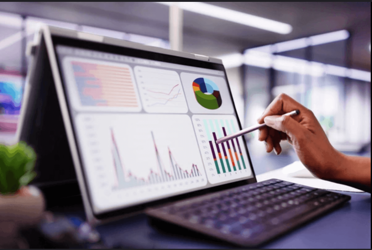 A person analyzing various colorful data charts and graphs on a computer screen with a stylus in a modern office setting.
