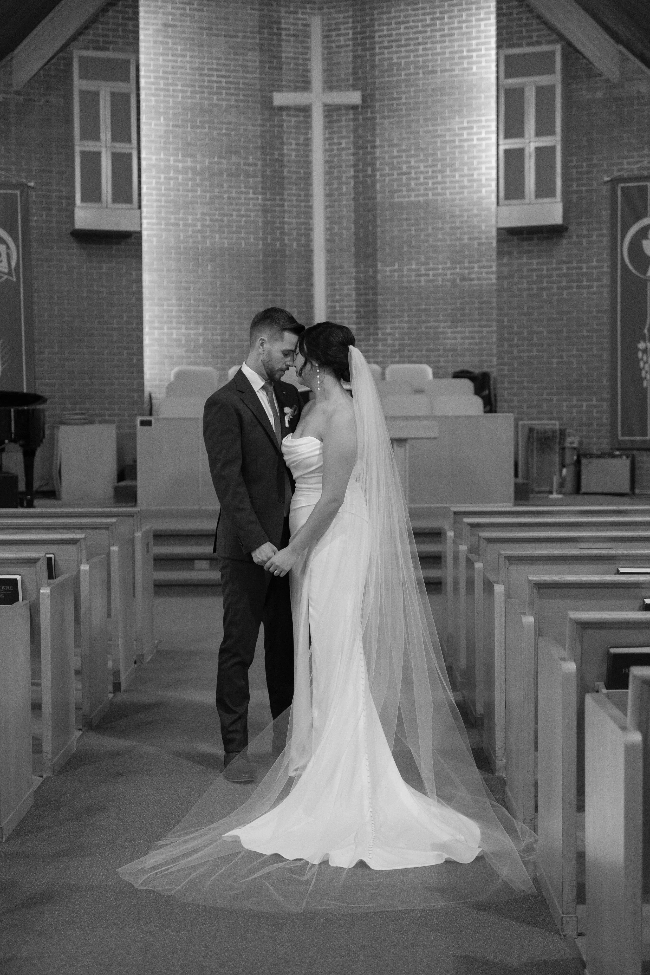 A bride and groom holding hands in a church, standing close with foreheads touching, during their wedding ceremony.