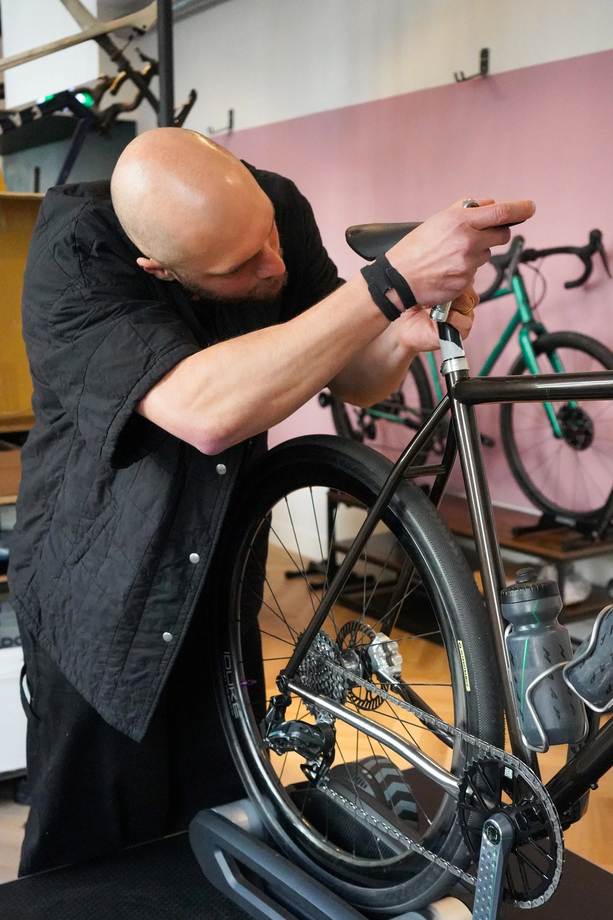 A man with a bald head and wearing a black shirt is working on a bicycle, adjusting or repairing the seat.