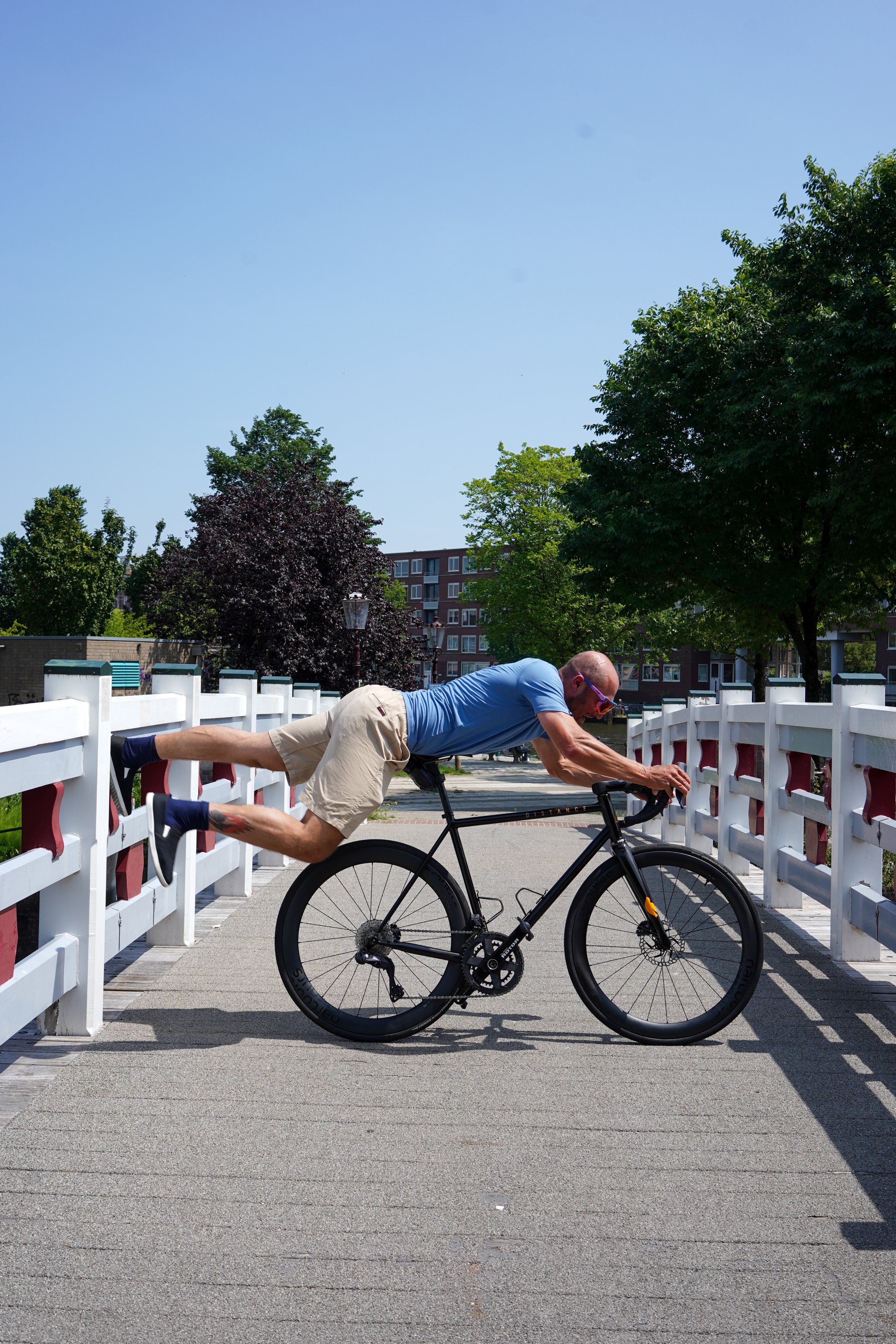 Man balancing on a bike while doing a horizontal plank on a bridge.