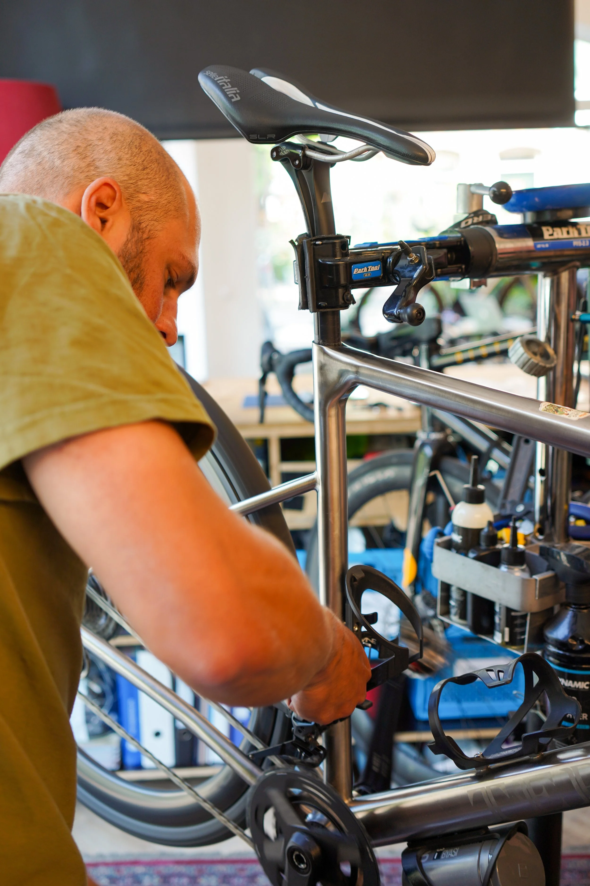 A person working on assembling or repairing a silver bicycle in a workshop, surrounded by tools and bike parts.