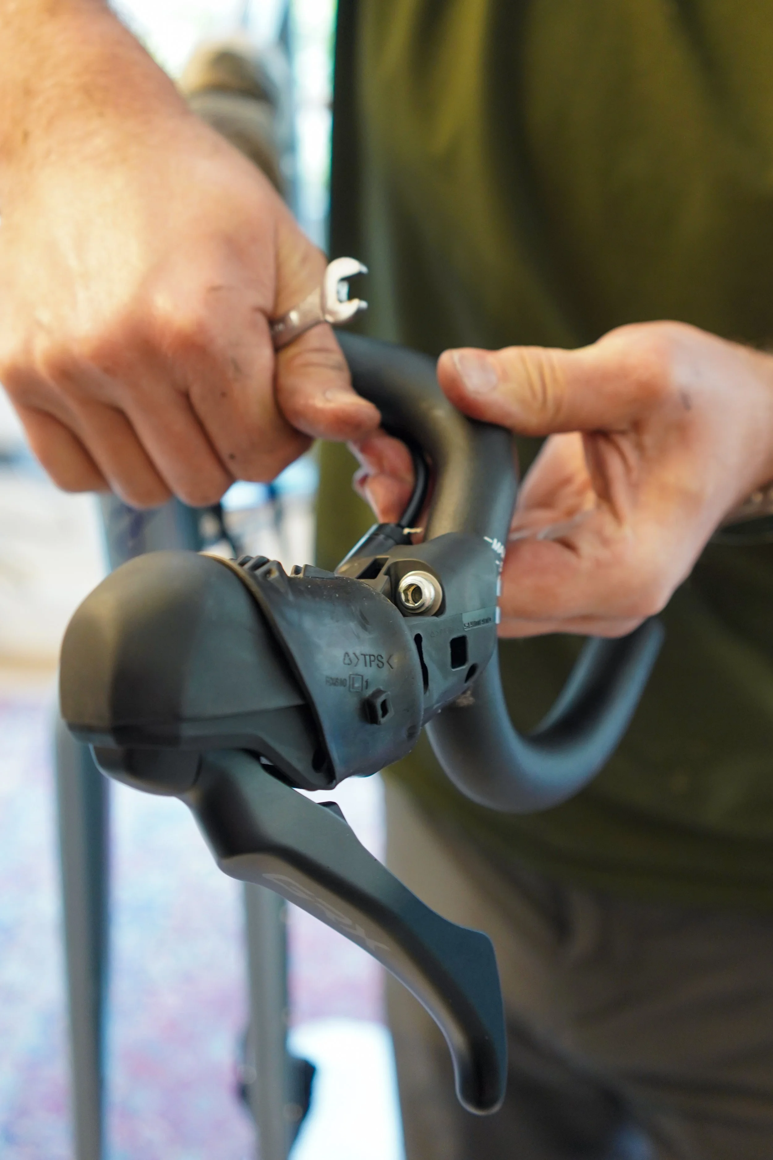 Close-up of a person's hands working on a bicycle's handlebar, attaching or repairing a gear shifter or brake lever.