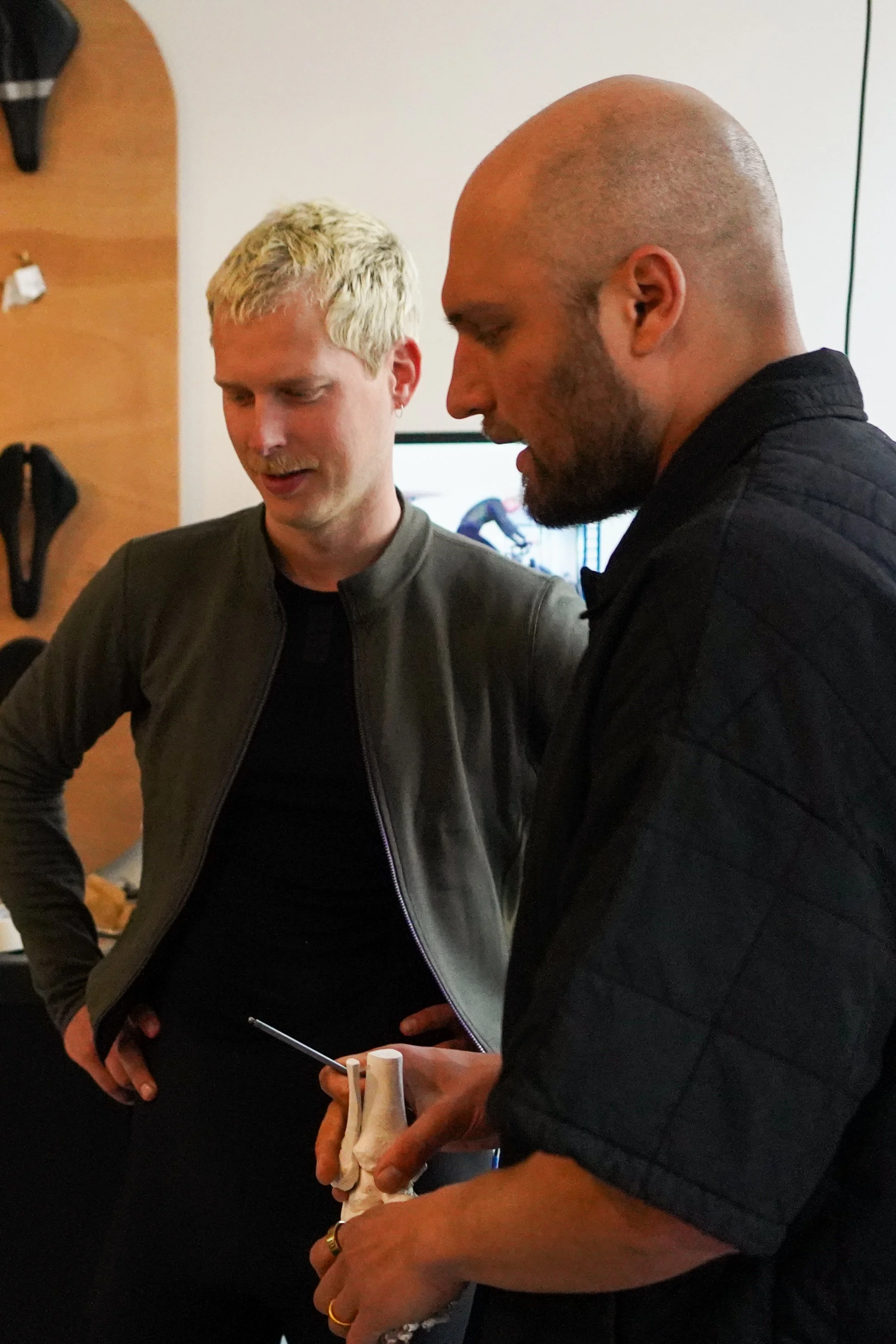 Two men engaged in a conversation, with one holding a model of a human ankle and foot. The man on the right appears to be demonstrating or explaining something related to the ankle model.