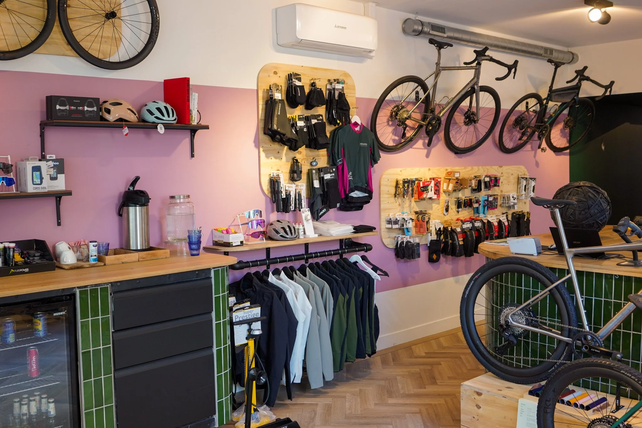 Inside a bicycle shop with bikes mounted on the wall, cycling gear on display, helmets on shelves, and clothing hanging on racks.