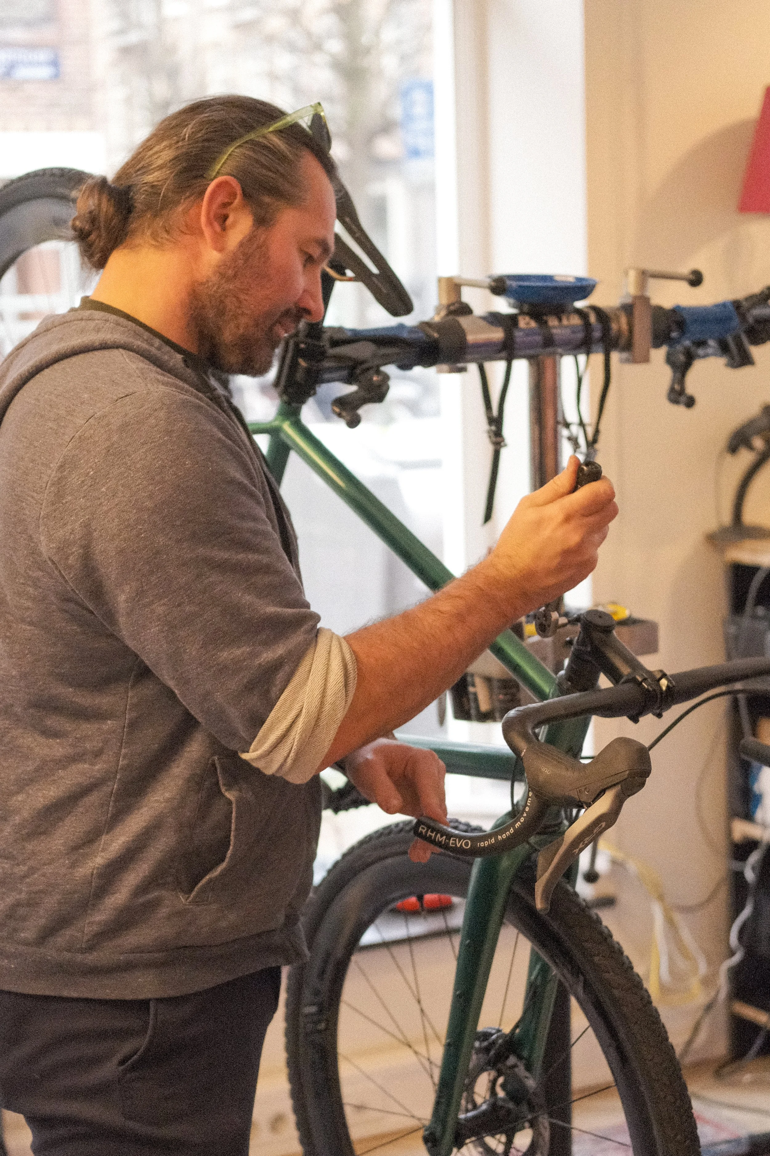 A man with long hair and a beard working on a mountain bike inside a bike shop.