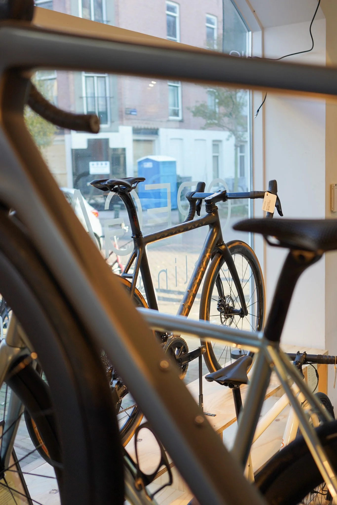 Two bicycles displayed inside a store near a large window, with a city street visible outside.