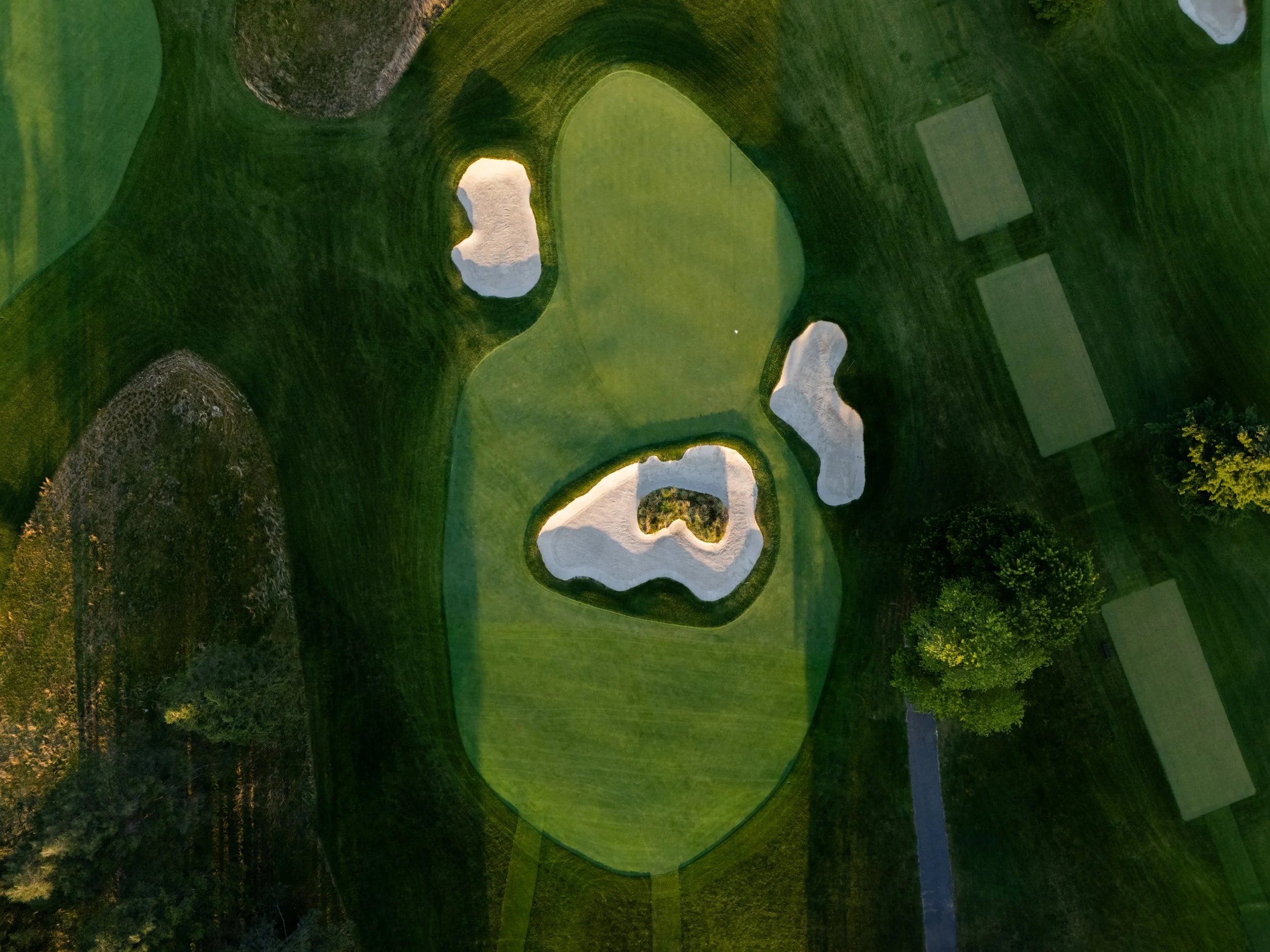Aerial view of a golf course with several sand bunkers and putting greens surrounded by grass and trees.