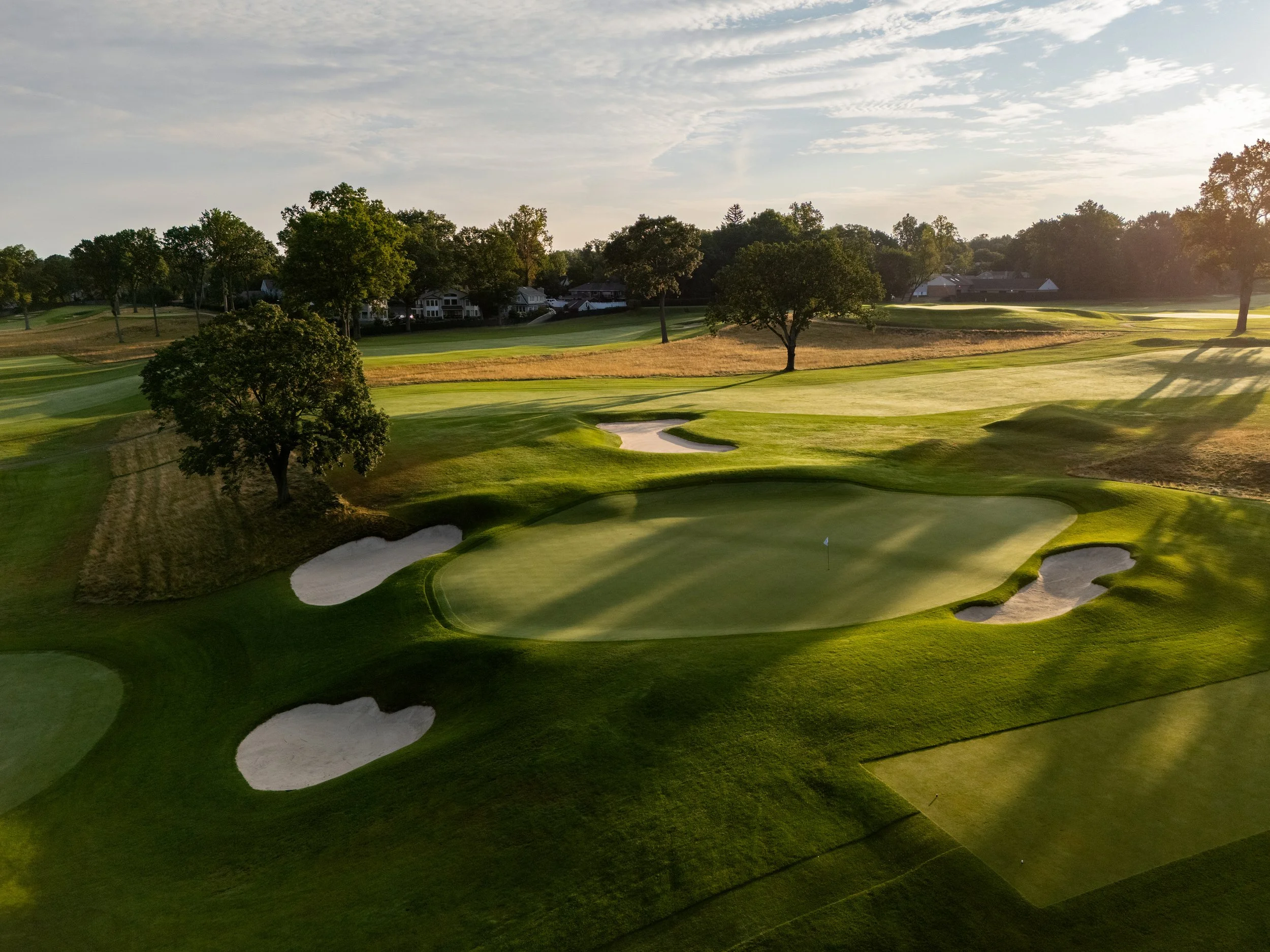 A golf course at sunset with green fairways, sand traps, and trees.