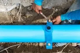 Person tightening a bolt on a blue pipe in a trench.