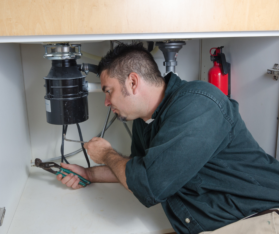 A man working under a kitchen sink using pliers and a wrench.
