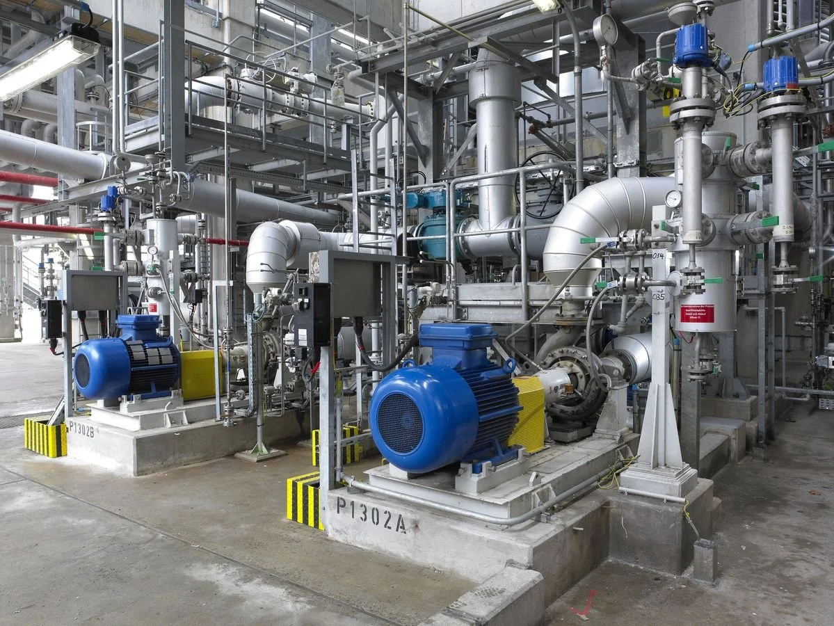 Industrial machinery with pipes, blue motors, and gauges in a factory setting.