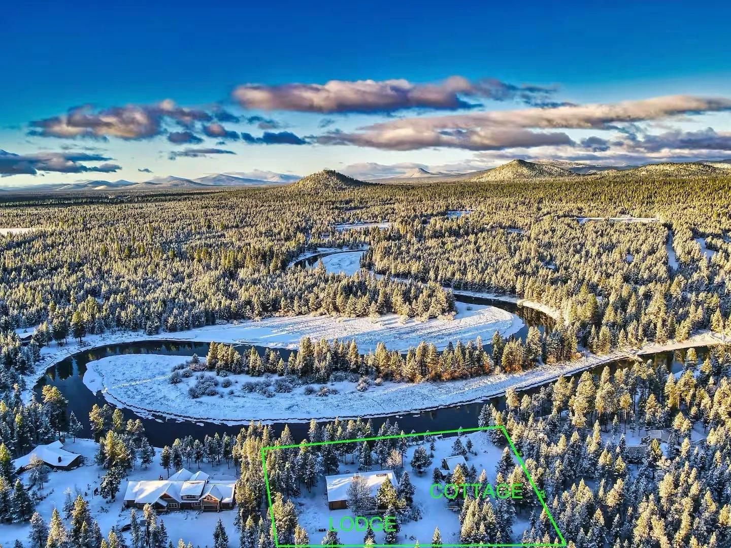 Aerial view of a snowy landscape with a meandering river, dense forest, mountains in the background, and a property outlined with a green border labeled 'LODGGE' and 'COTTAGE'.