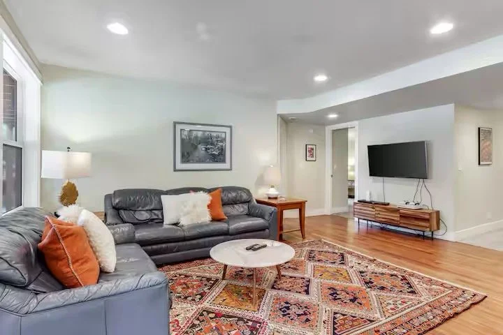 Living room with two leather sofas, a patterned rug, a round coffee table, a wall-mounted TV, and picture frames on the wall.
