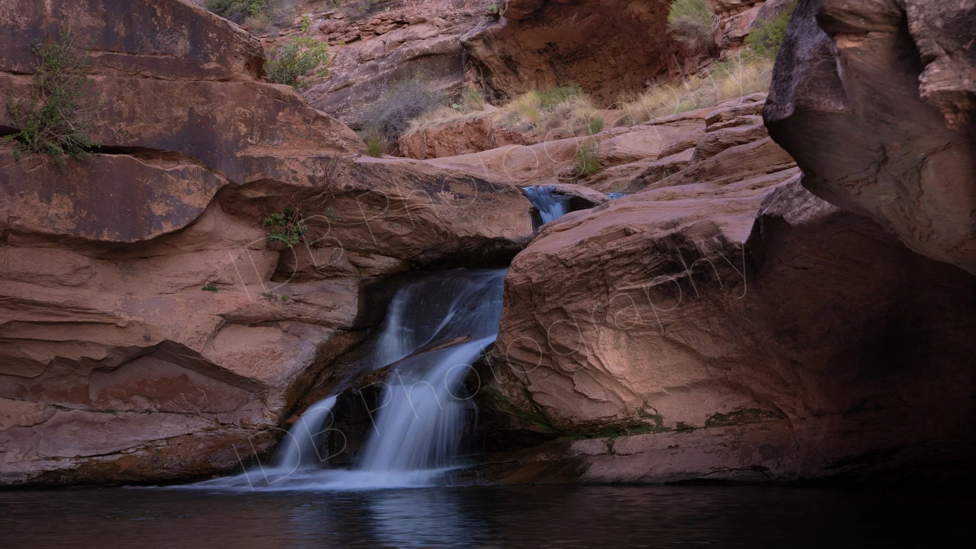 Mill Creek Waterfall, a peaceful scenic desert cascade in evening light, water cascades between the large reddish brown rocks.