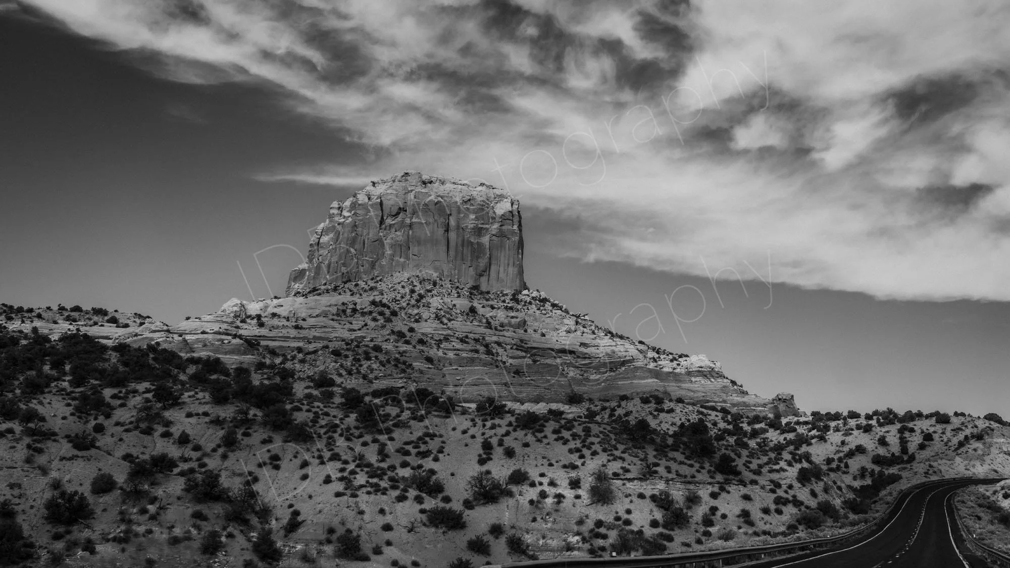 A black and white image of Square Butte, Arizona, a massive sandstone summit rises out of the scrubby desert terrain, adjacent to State Route 98.