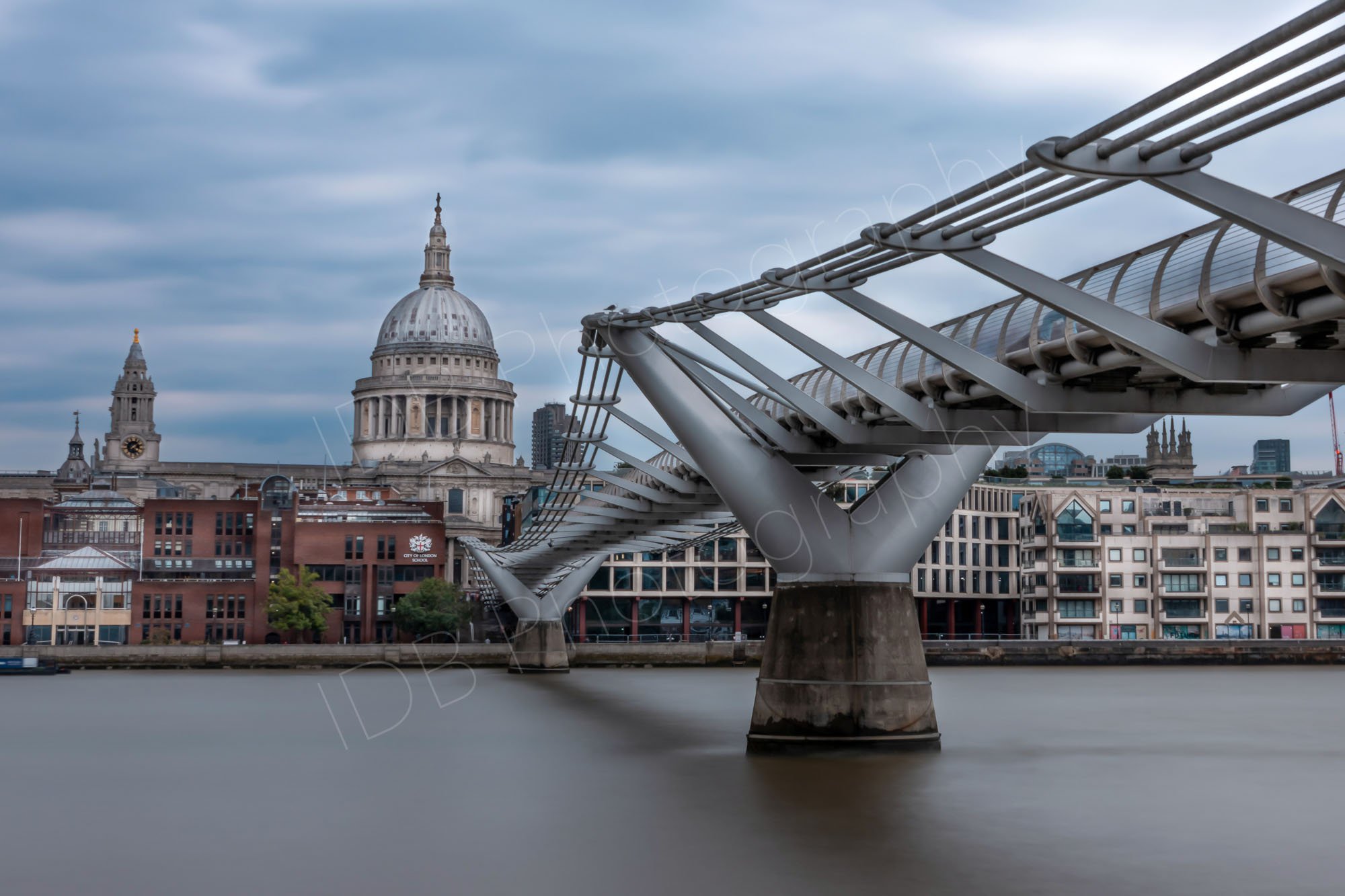 A long ND filter exposure across the Thames with the Millennium Bridge and St Paul's Cathedral clearly seen; smooth water and blue and white "fluffy" sky.