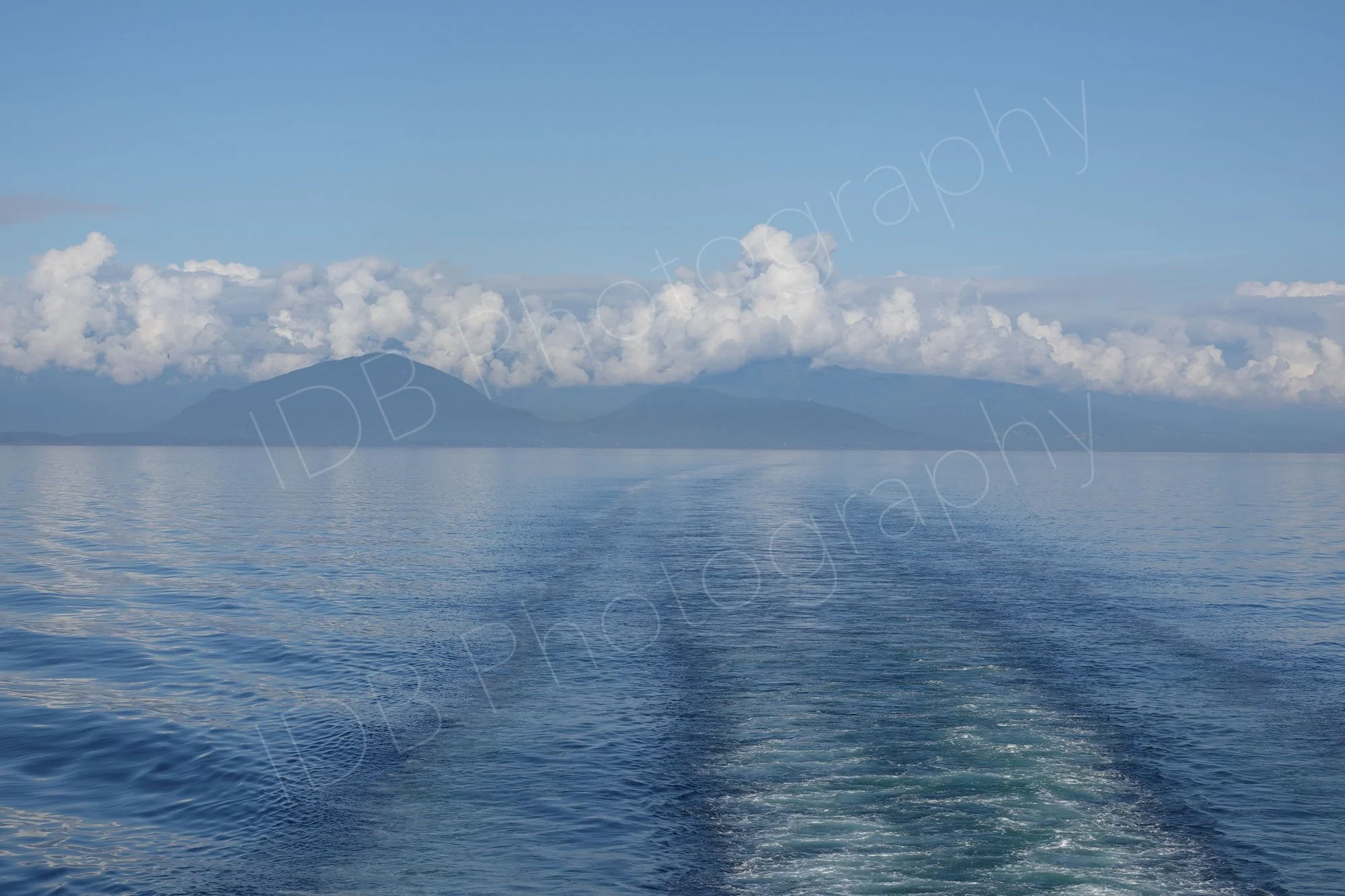 A peaceful image of  a calm Johnson's Straight broken only by boat wake lines; low mountains and cloud in the distance; BC, Canada. 