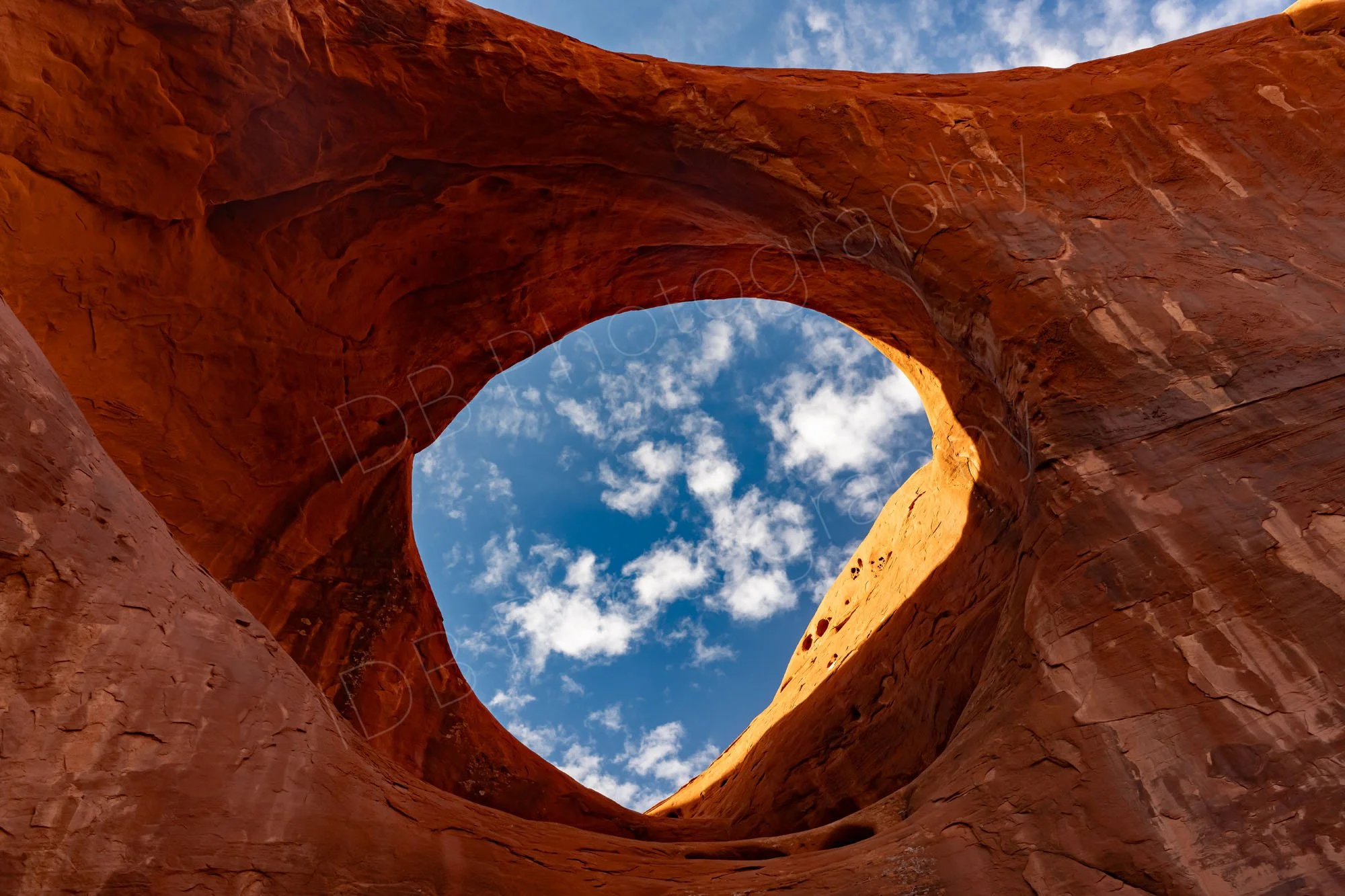 A rocky window and arch In Monument Valley Navajo Tribal Park, Utah, with bright cloudy blue sky.
