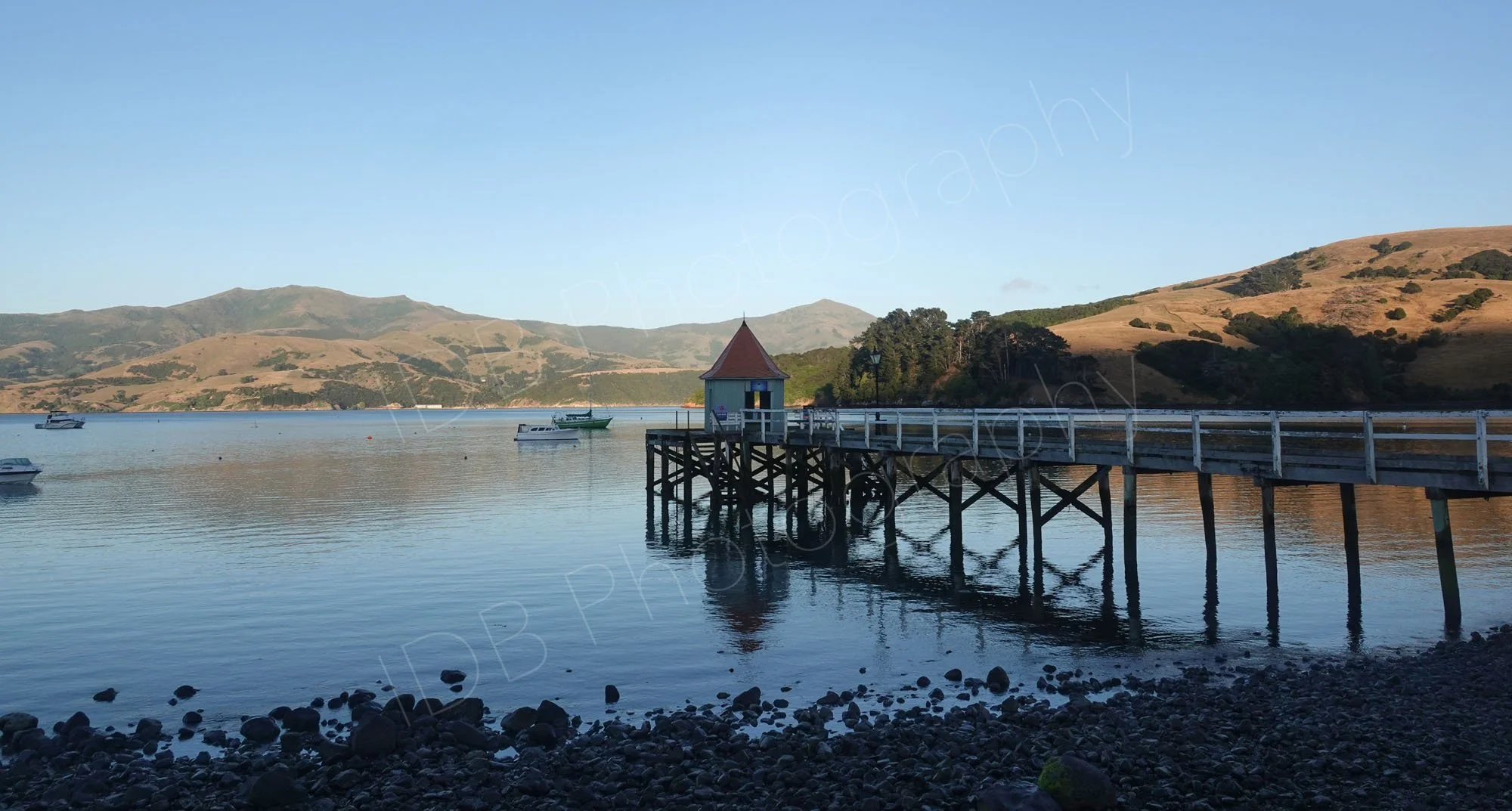 Old Pier in evening light with reflections in the water and hilly backdrop at Akaroa, Banks Peninsula, New Zealand.
