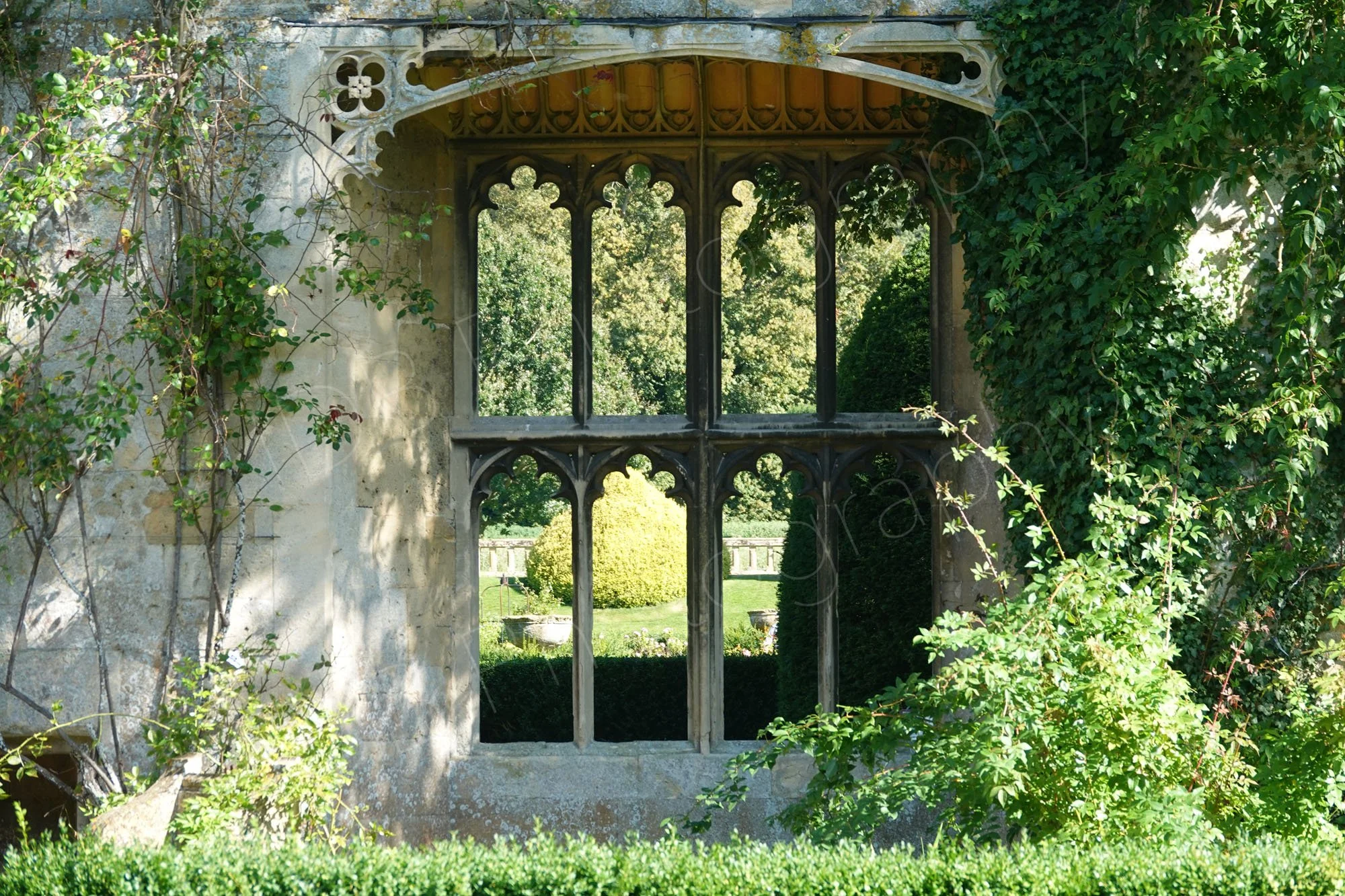A view through a weathered stone window frame to the gardens beyond at the 15th-century ruins at  Sudeley Castle in Gloucestershire.